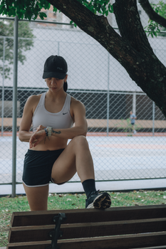 A woman in athletic wear checks her smartwatch while exercising outdoors near a tennis court.