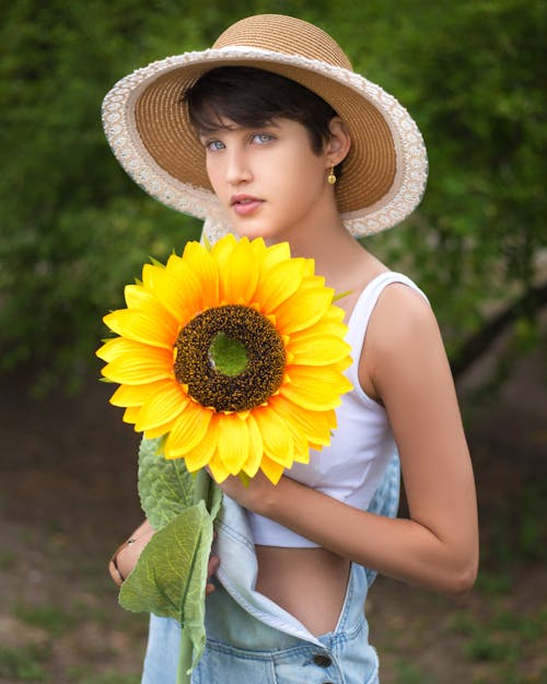Free Woman in Yellow Sun Hat and White Tank Top Holding Sunflower Stock Photo