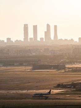 Panoramic view of Madrid skyline with airplane taxiing at sunset, capturing urban and aviation elements.