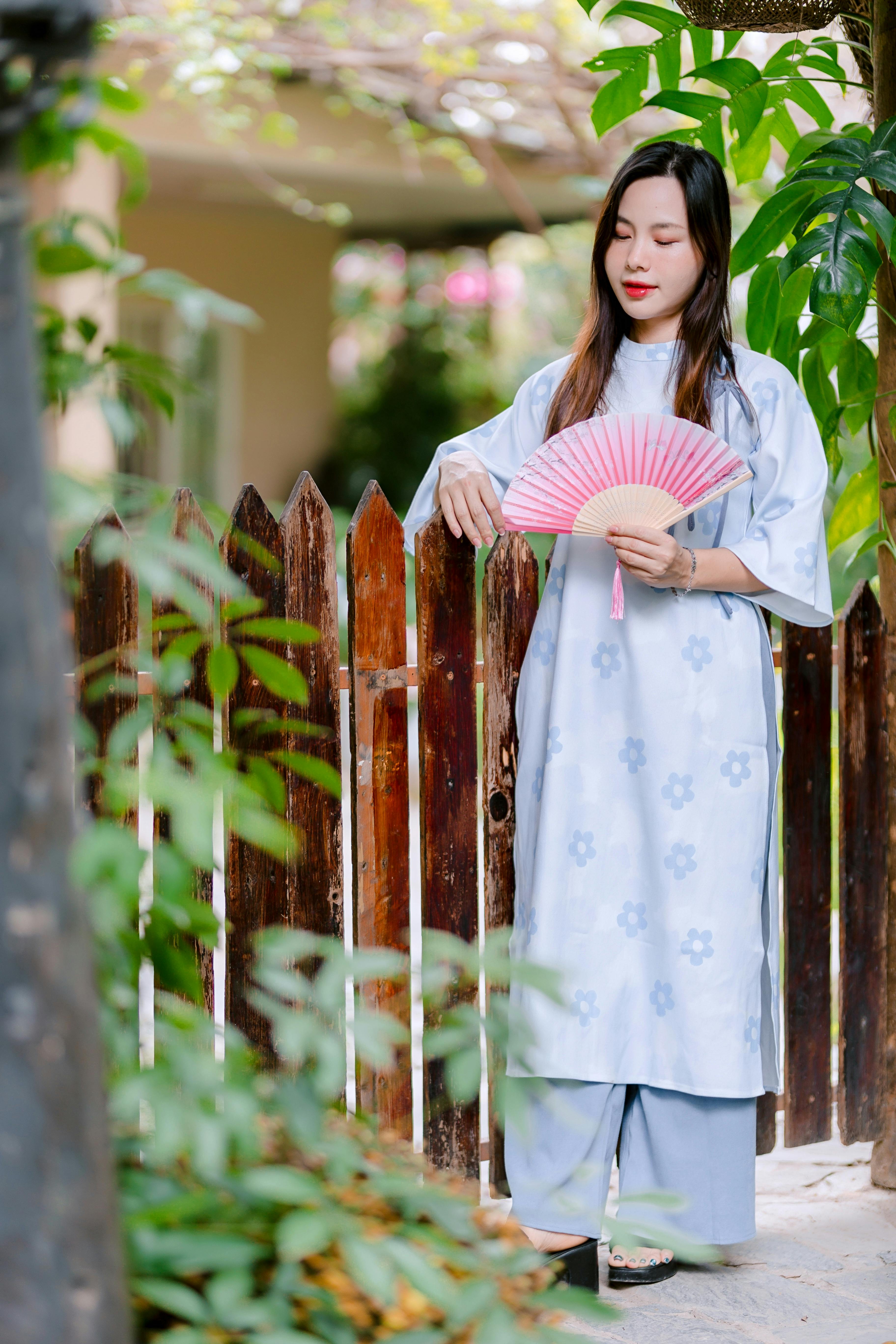 Gratis Frau in Traditionaleller Kleidung mit rosa Fächer, draußen im Garten. Foto a disposizione