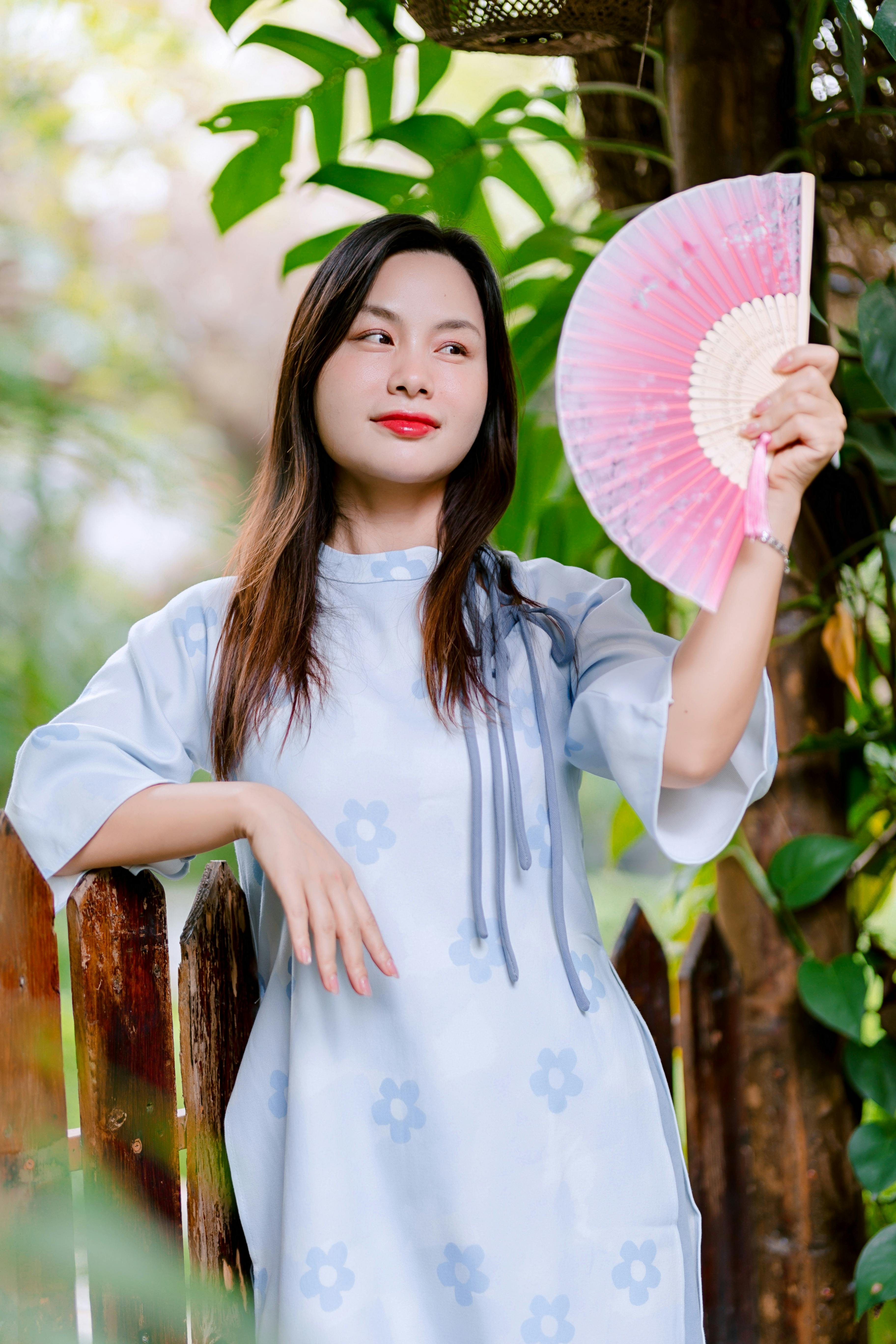 Gratis Una donna in abito elegante tiene in mano un ventaglio all'aperto, emanando un'atmosfera serena e raffinata. Foto a disposizione