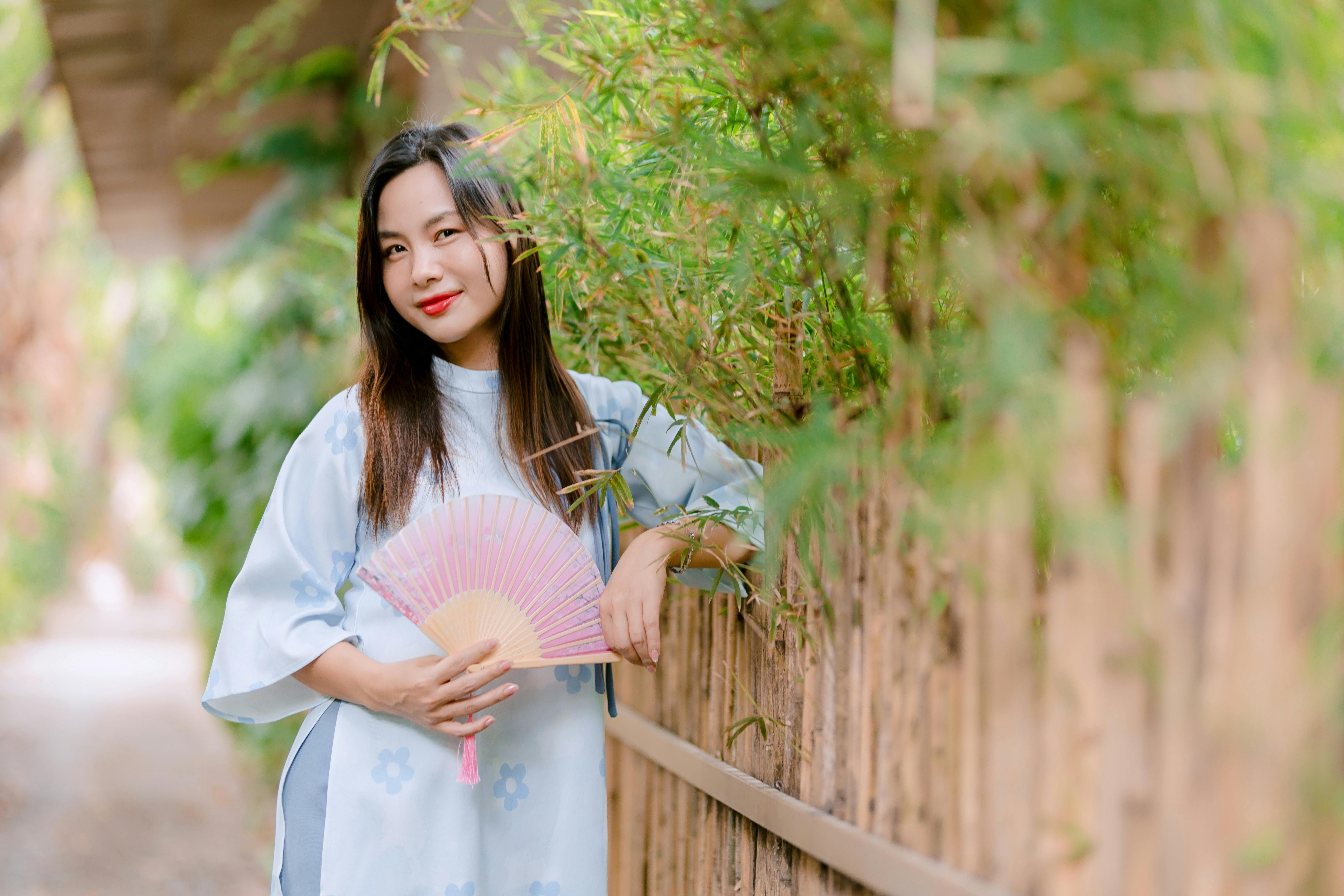 無料 伝統的な衣装を身にまとった女性が、竹林のそばで扇子を持っている。静かで優雅な光景だ。 写真素材