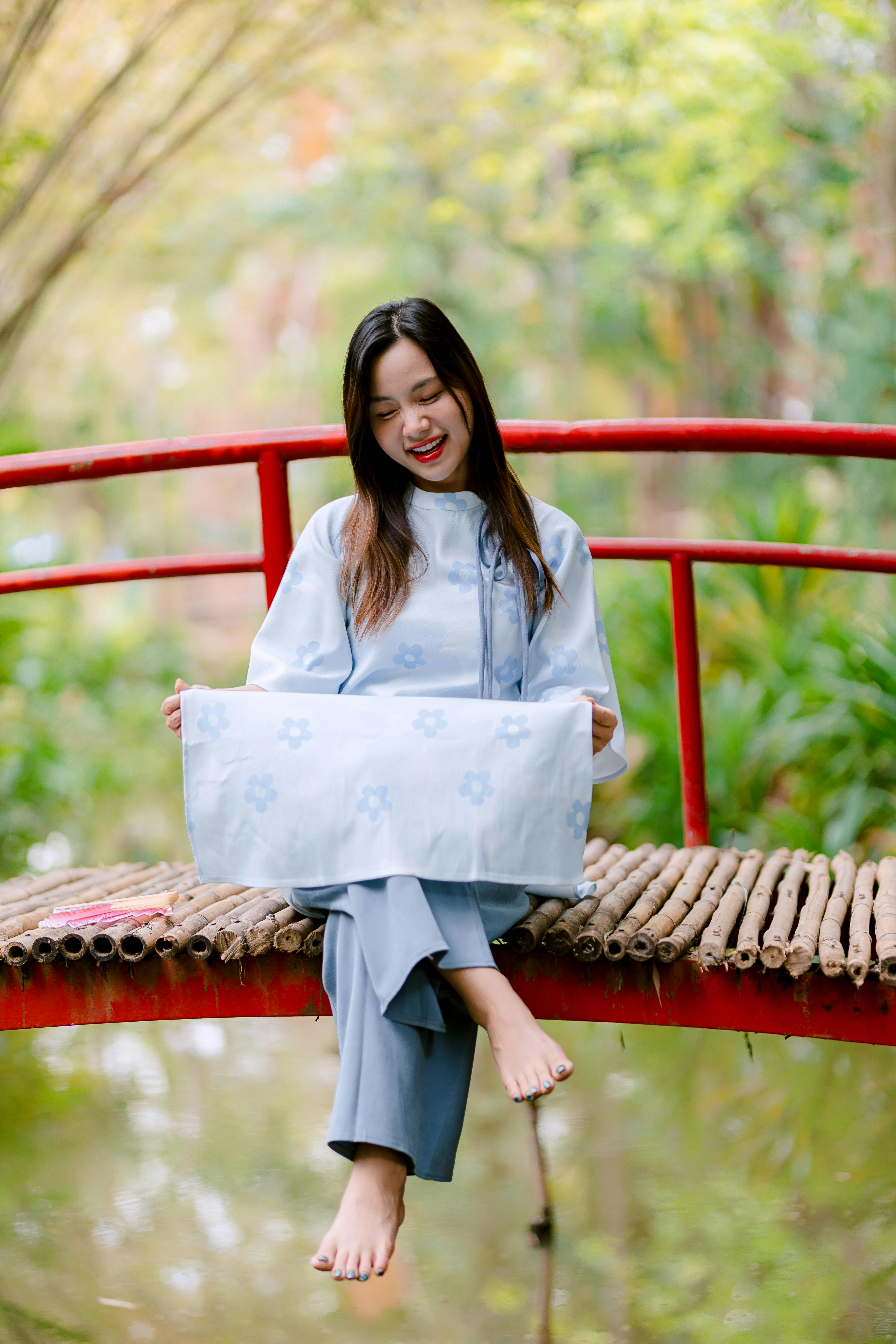 無料 赤い橋の上に座って、自然の中で穏やかなひとときを楽しんでいる若い女性。 写真素材