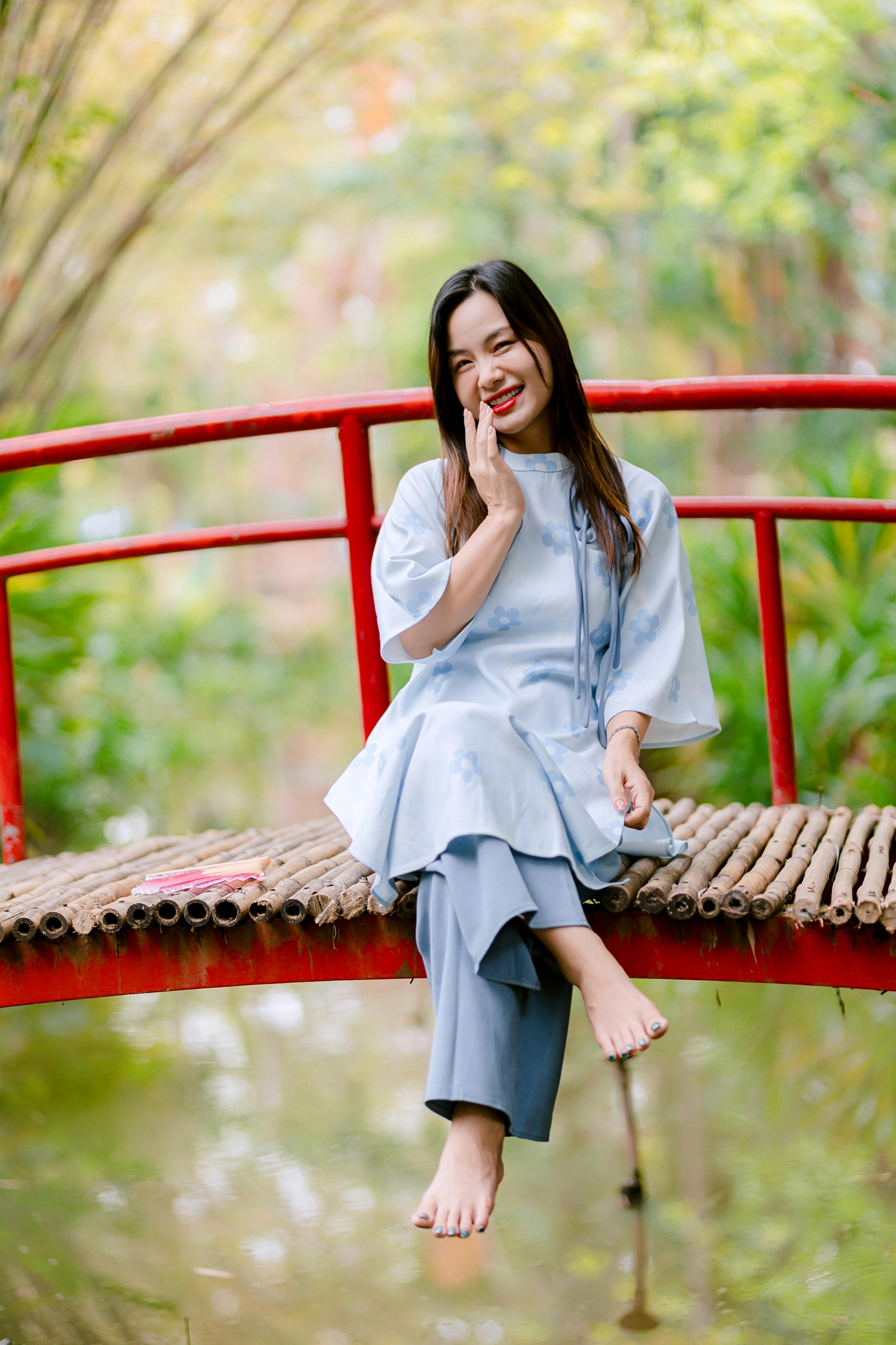 Ücretsiz Sakin bir açık hava ortamında bambu köprü üzerinde oturan gülümseyen bir kadın. Stok Fotoğraflar