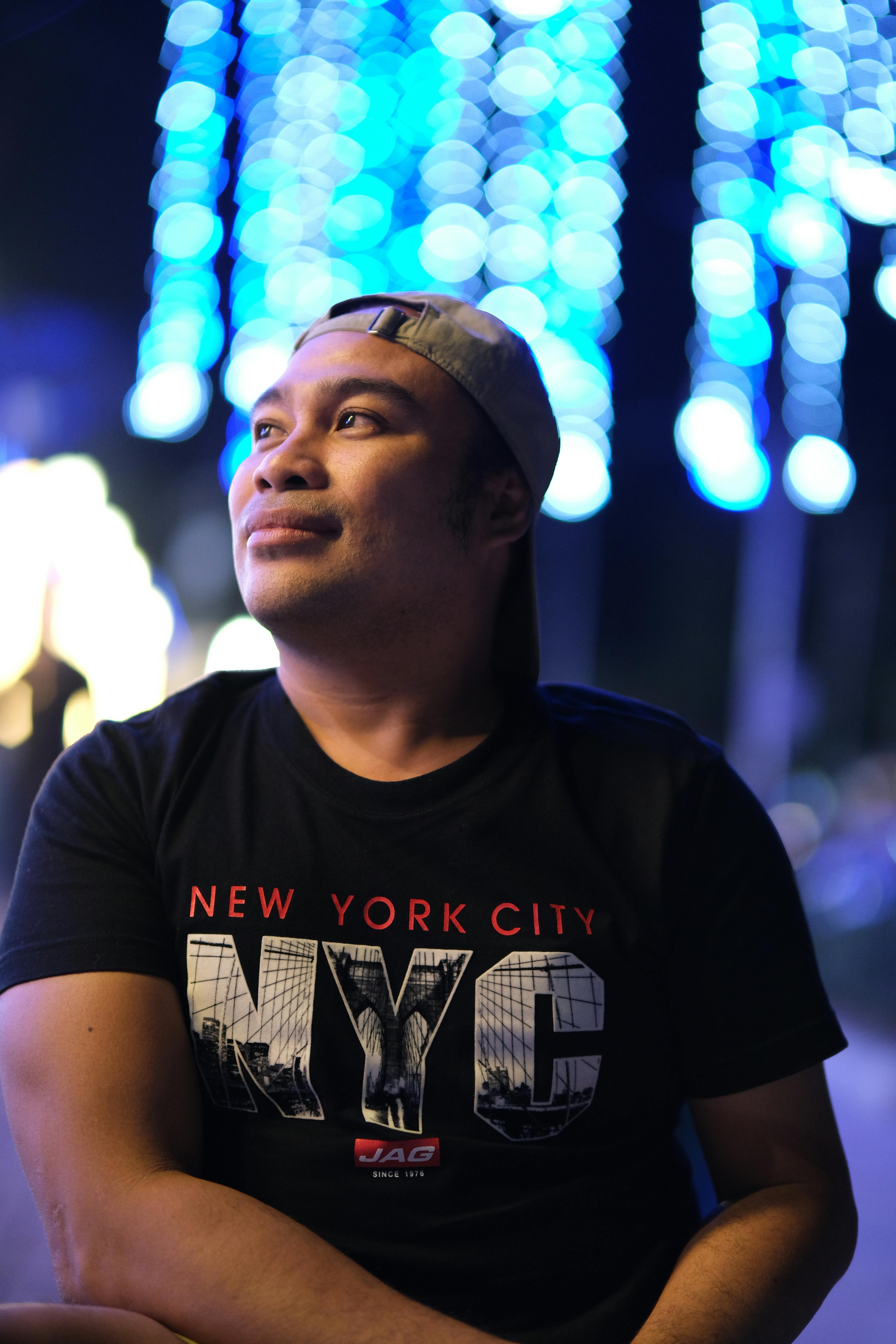 Man in casual attire gazing thoughtfully under vibrant blue festive lights.