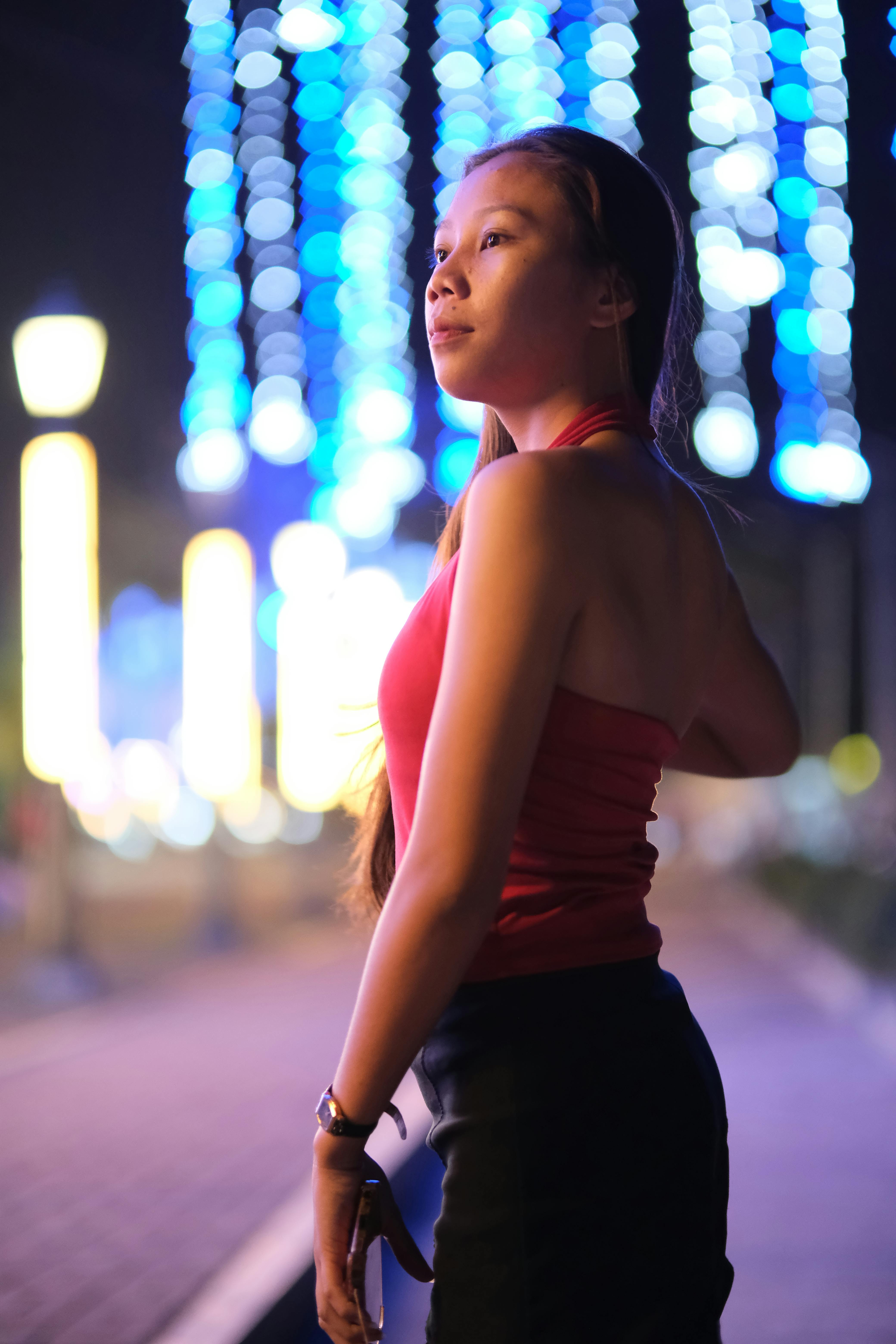 Gratuit Une femme en robe rouge pose en extérieur, de nuit, avec les magnifiques lumières de la ville en arrière-plan. Photos