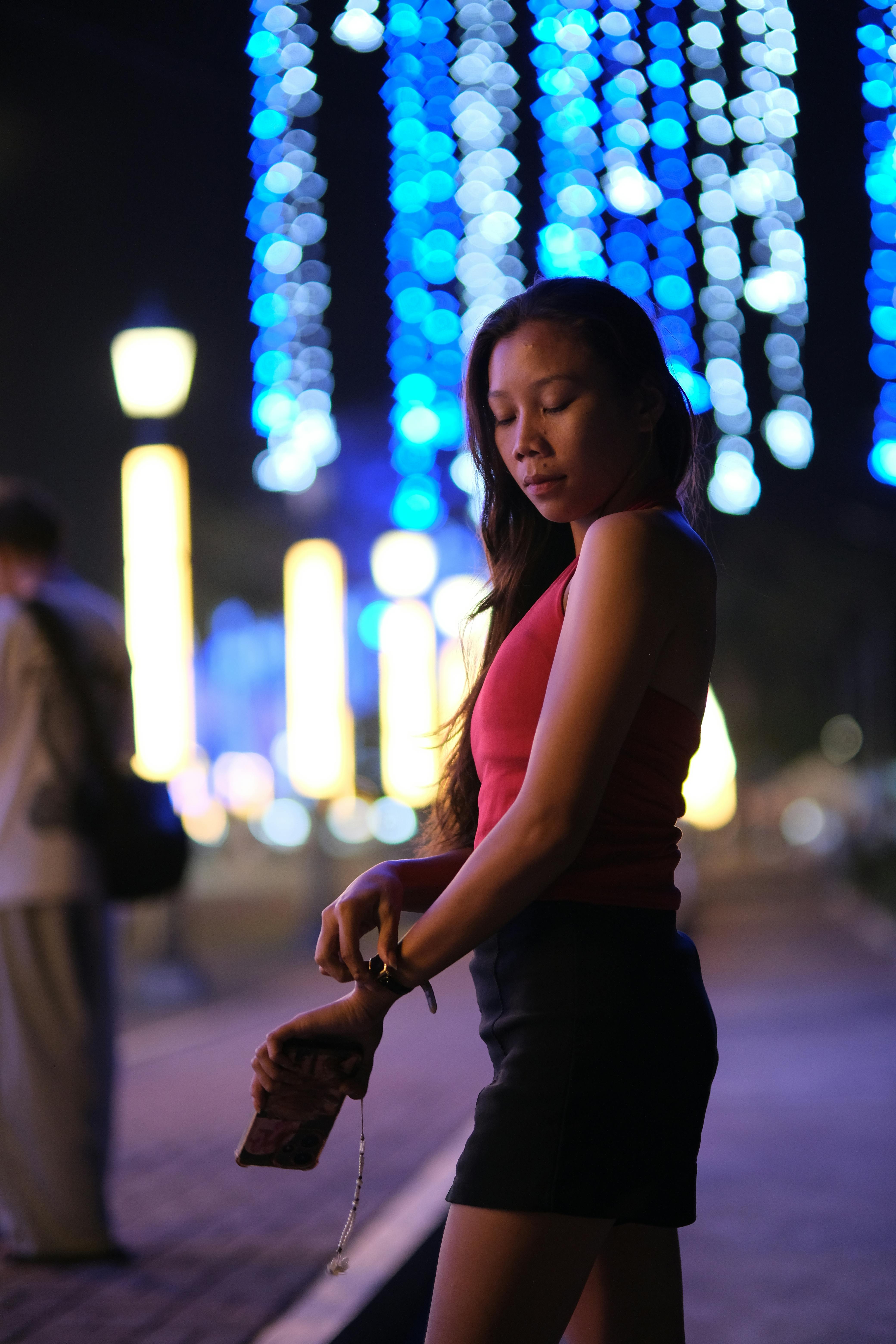 Gratis Ung kvinde poserer elegant om natten med farverige festlige lys i baggrunden, hvilket skaber en bokeh-effekt. Lagerfoto