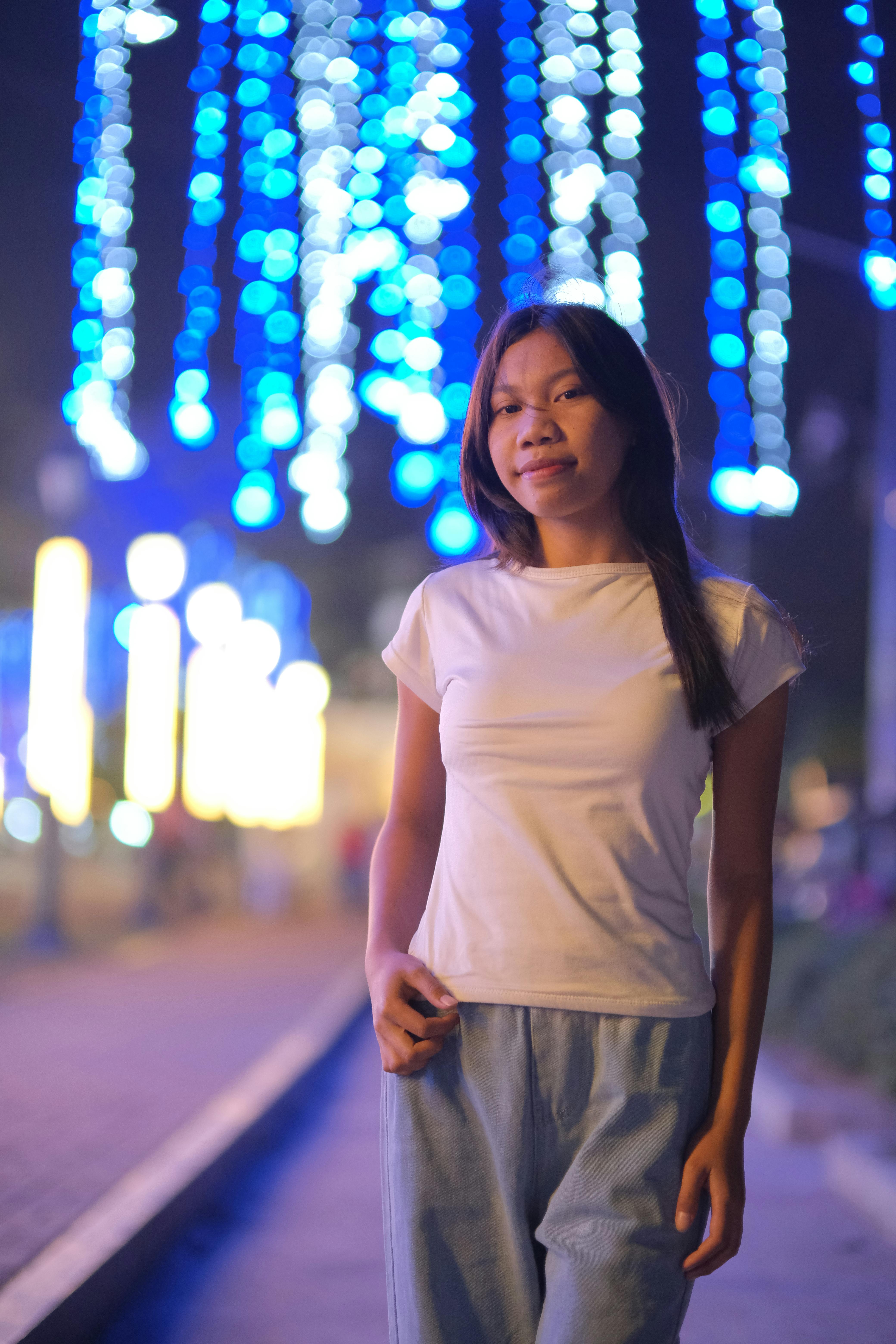 Ücretsiz Günlük kıyafetler giymiş genç bir kadın, geceleyin canlı mavi ışıklar altında dolaşıyor. Stok Fotoğraflar