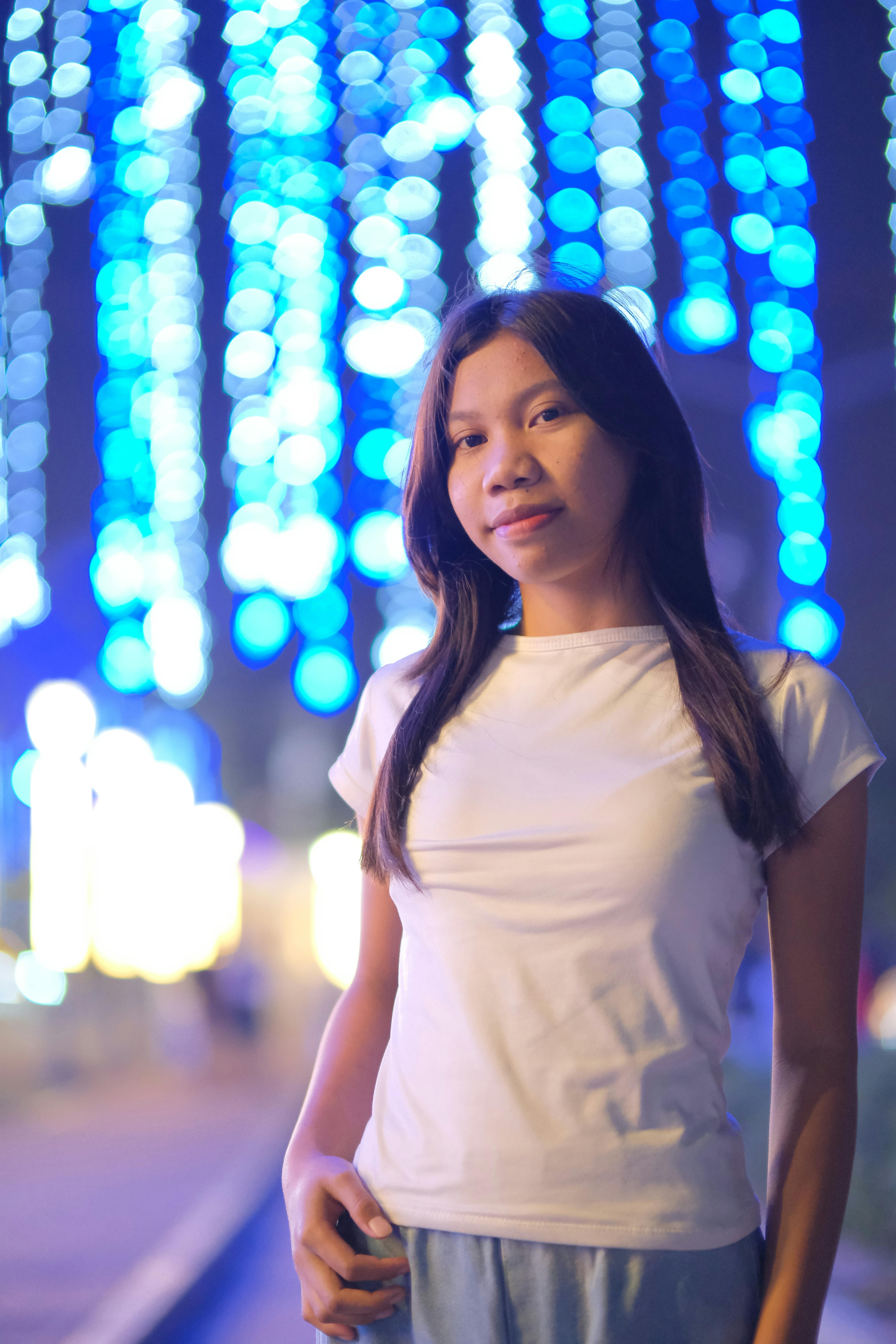 Gratis Ritratto di una giovane donna sicura di sé all'aperto di notte, con vivaci luci blu sullo sfondo. Foto a disposizione