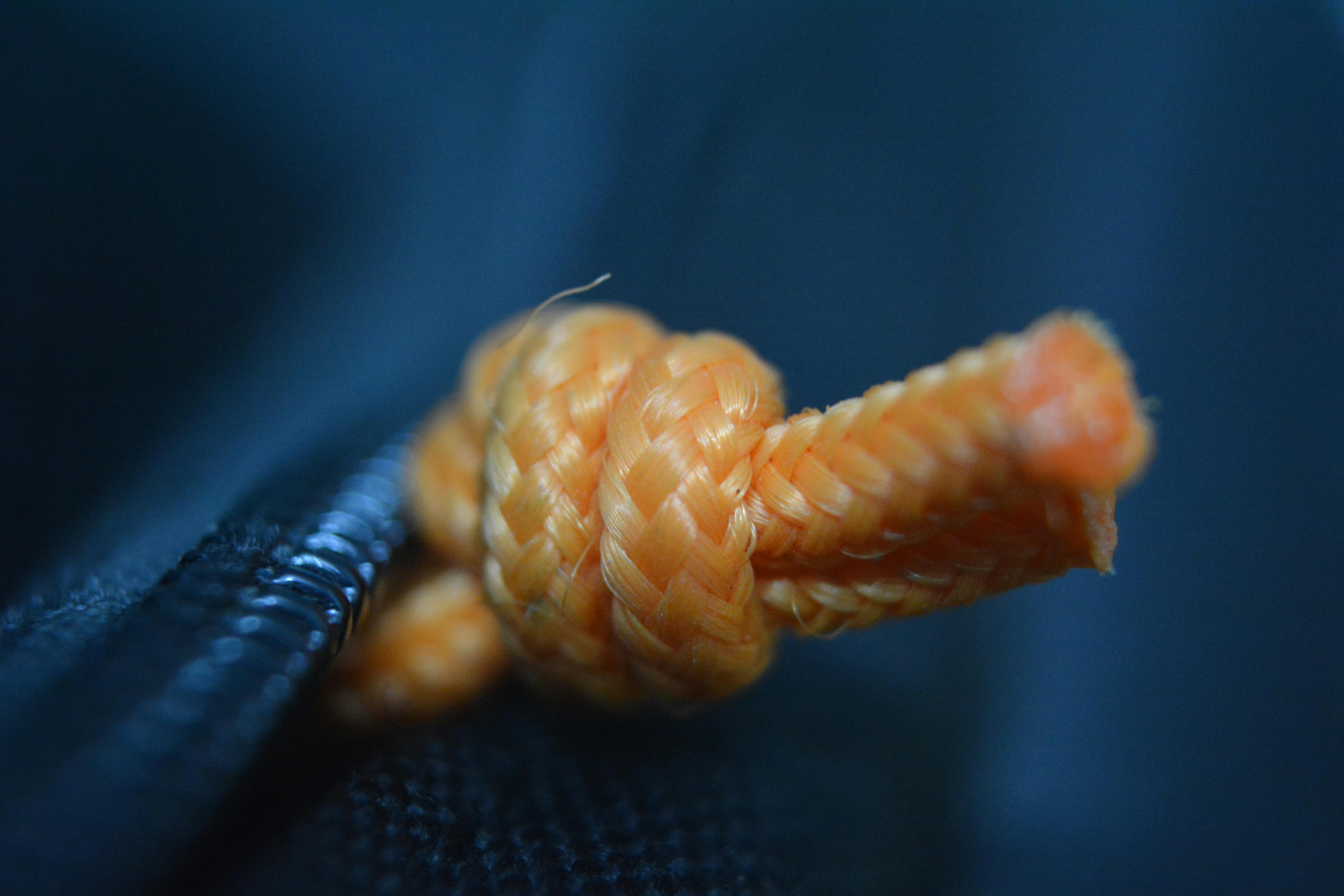 grátis Detalhe em close-up de um nó de corda laranja contra um fundo escuro, evidenciando sua textura. Foto profissional