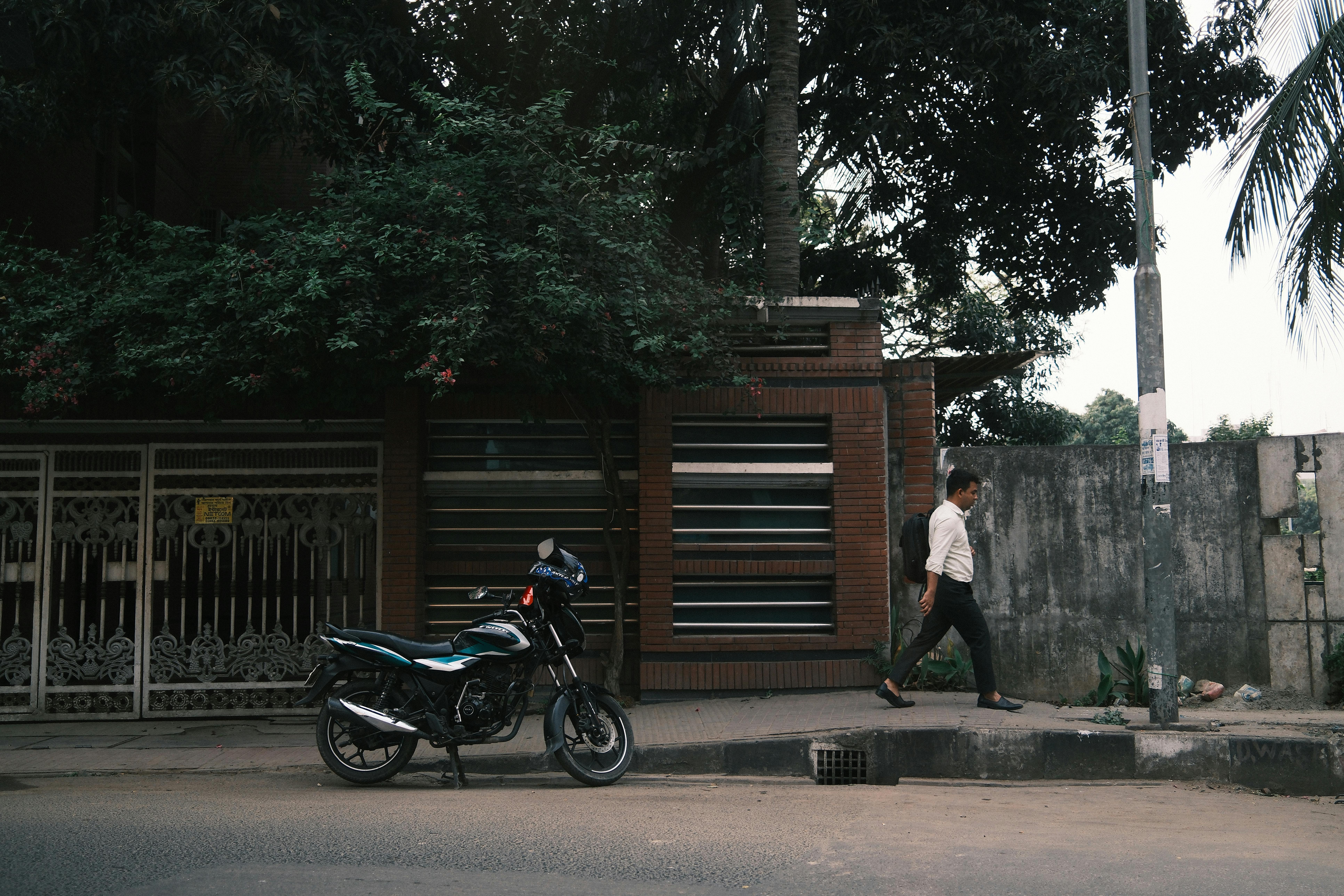 Gratuit Un bărbat trece pe lângă o motocicletă parcată pe o stradă urbană, surprinzând viața orașului. Fotografie de stoc