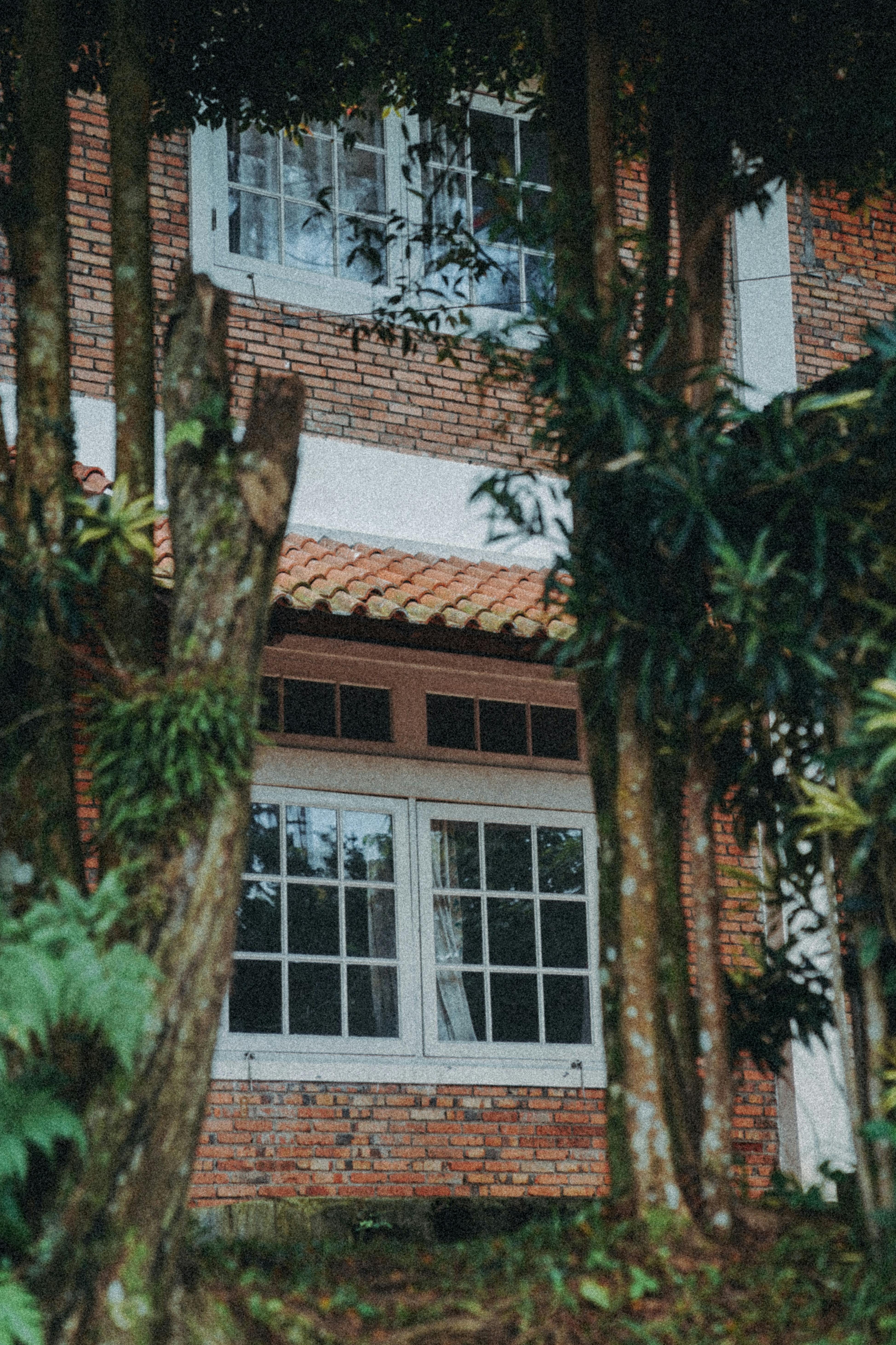 Gratuit Vue extérieure d'une maison en briques encadrée par des arbres à Cisarua, en Indonésie, créant une atmosphère rustique. Photos