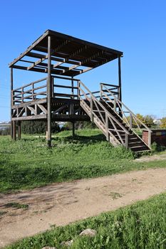 A wooden observation deck in a grassy area under a clear blue sky in El Puerto de Santa María, Spain.