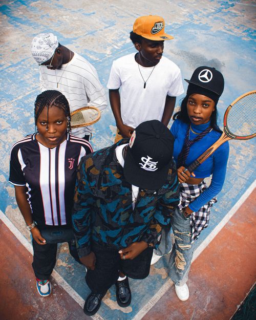 Free Five youths posed on a worn tennis court, holding rackets, in casual streetwear. Stock Photo