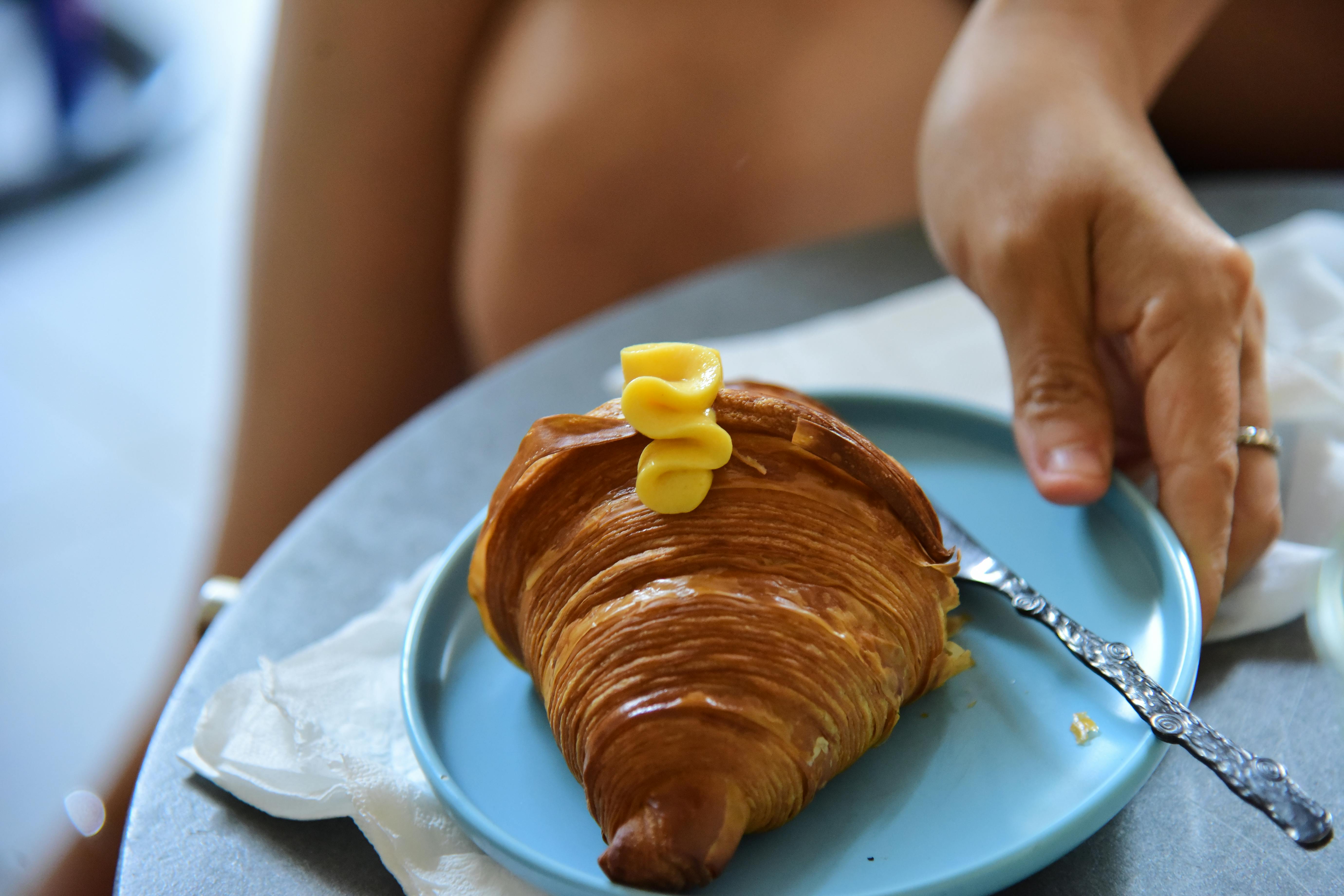 Gratis Un croissant appena sfornato, spalmato di burro e servito su un piatto blu. La colazione perfetta. Foto a disposizione