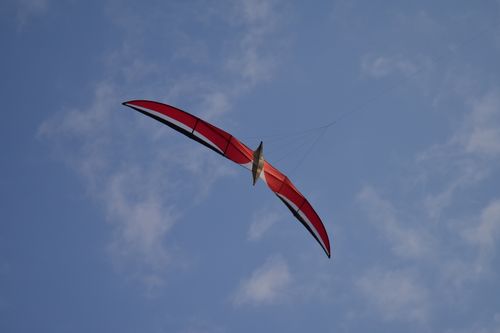 Free A red hang glider gracefully flying against a clear blue sky with soft clouds. Stock Photo
