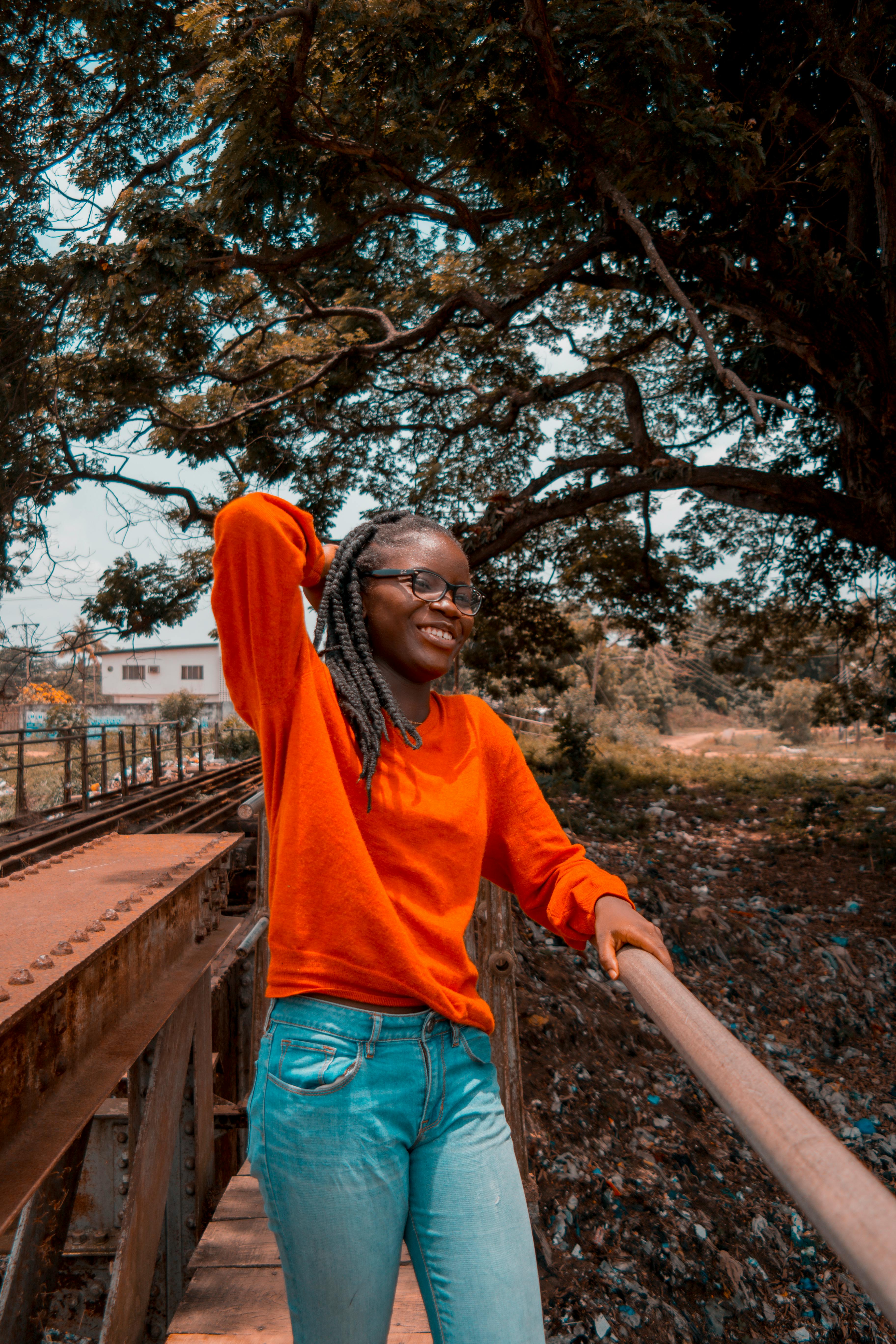 一位身着橙色运动衫的自信女性，在户外的桥上摆出姿势，捕捉轻松时尚的氛围