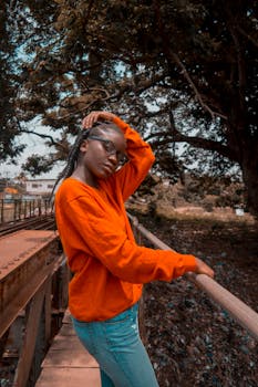 一名身穿橙色毛衣的黑人女子，在自然户外背景下自信地摆出姿势