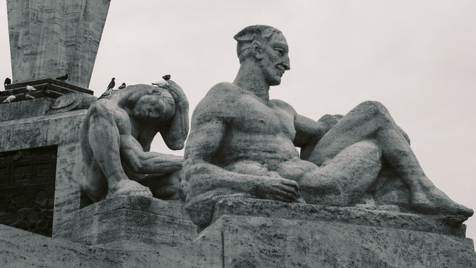 Artistic shot of large stone statues with birds perched on a monumental structure.