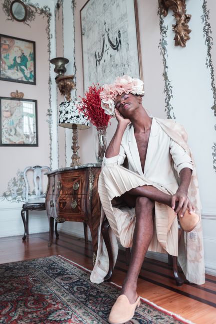 Stylish man wearing a flower crown in a vintage room setting, evoking artistic elegance.