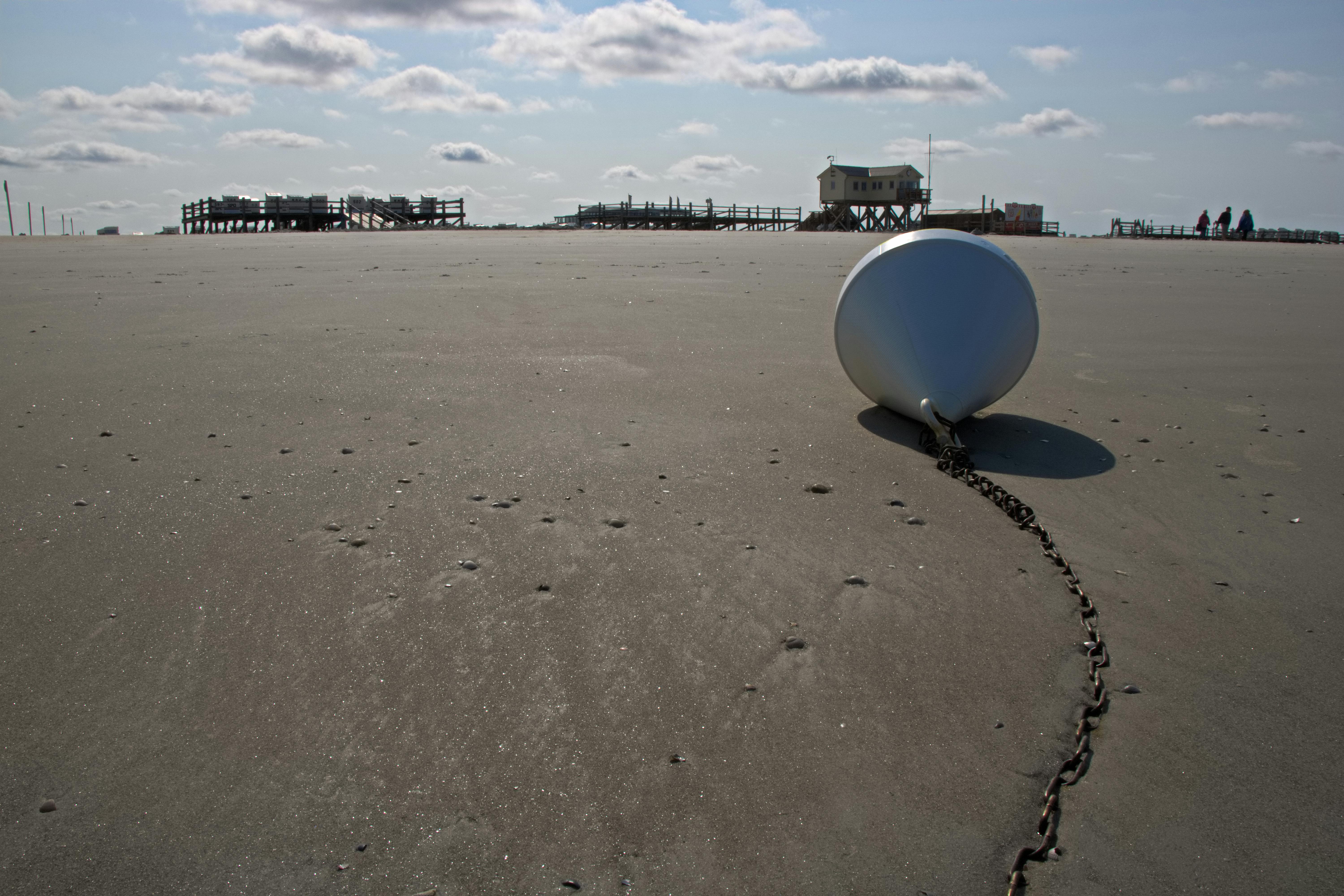 無料 晴れ渡った空の下、広い砂浜にぽつんと浮かぶブイと、遠くに見える桟橋。 写真素材