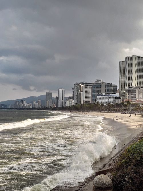 Free A striking view of Vietnam's coastline with powerful waves and a modern city skyline. Stock Photo