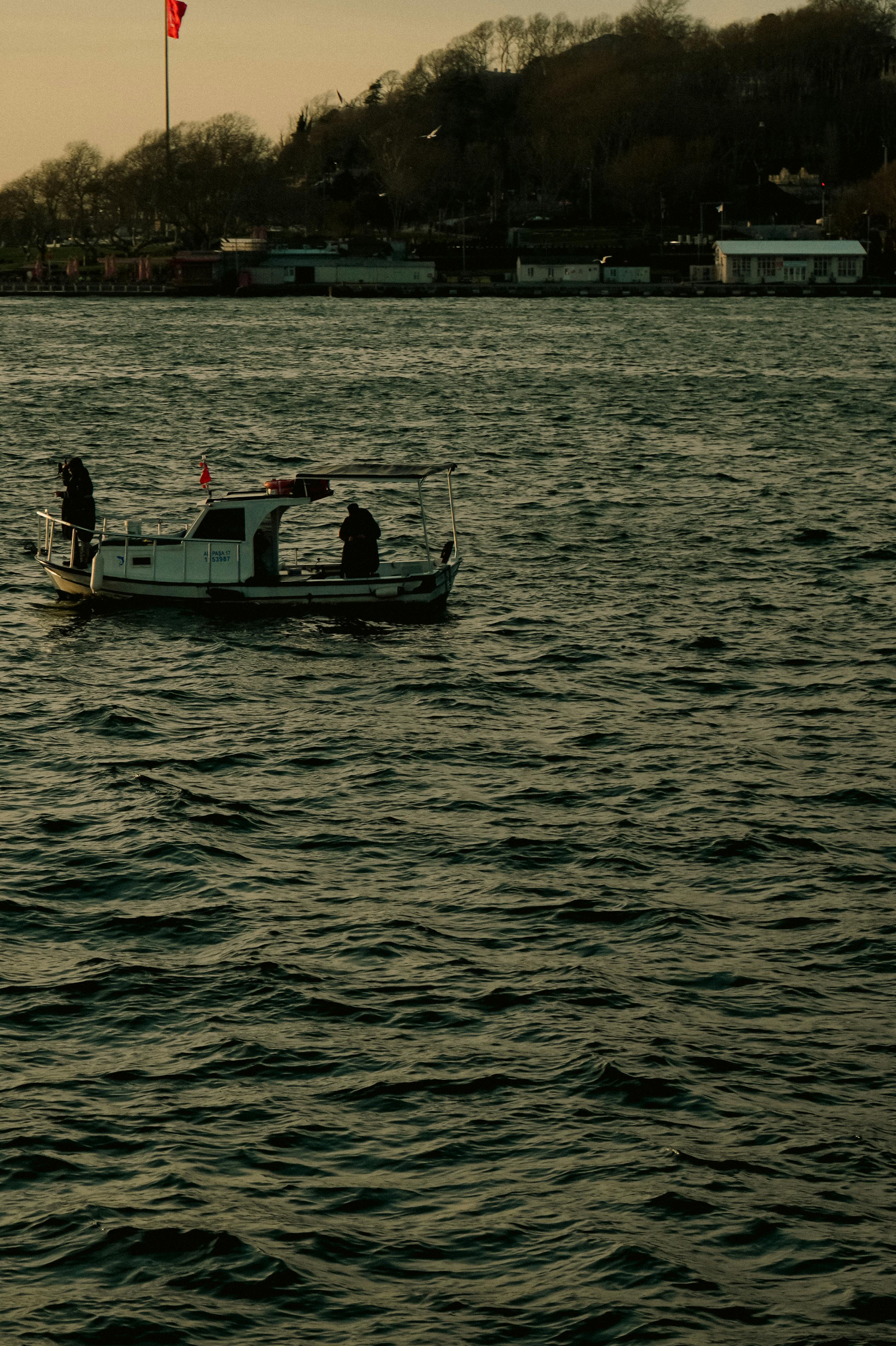 Zadarmo Malá loď s dvoma osobami plaviacimi sa po pokojnej vodnej ploche počas západu slnka. Fotka z fotobanky