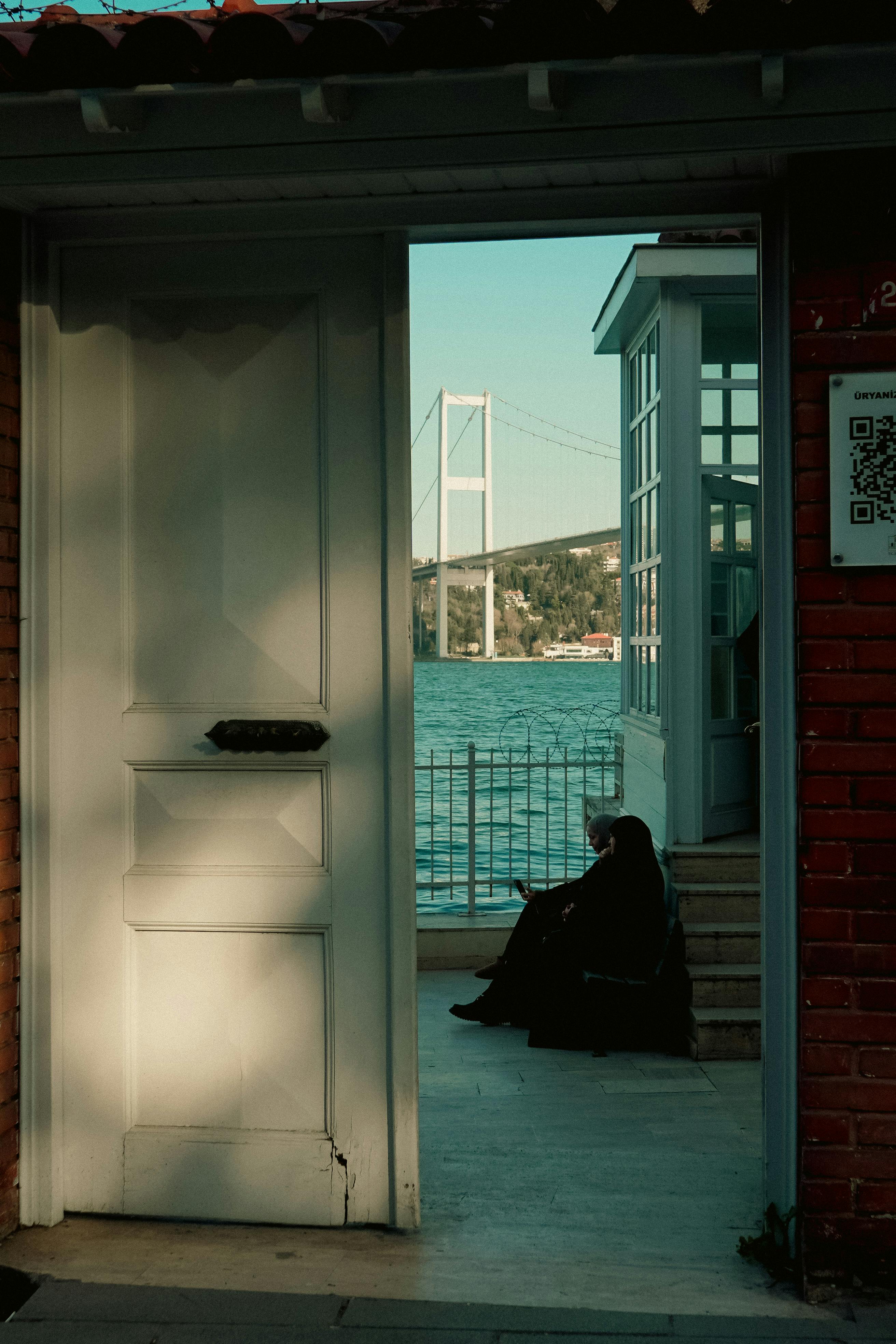 ingyenes Személy ül az isztambuli Boszporusznál, kilátással a hídra az ajtón keresztül naplementekor. Stockfotó