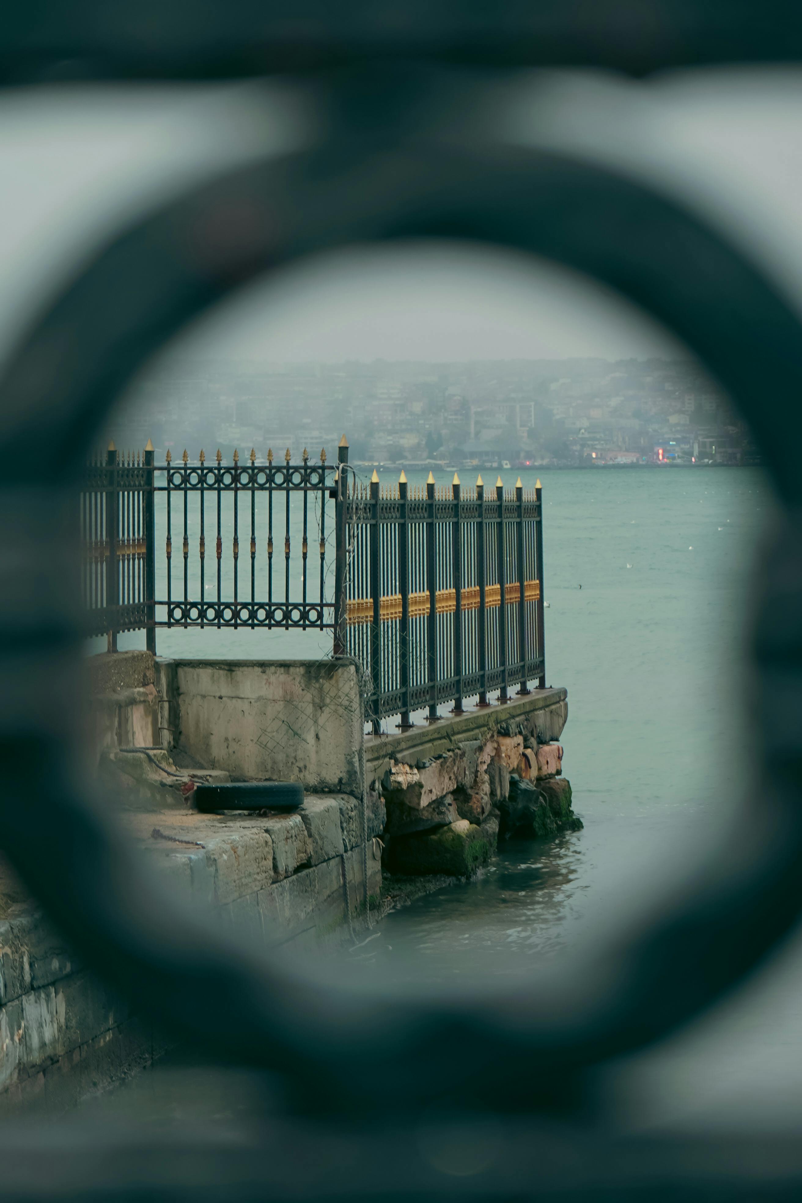 免費 透過圓形鐵藝，以獨特的視角展現碼頭和欄桿，捕捉到一幅充滿意境的海濱景象。 圖庫相片