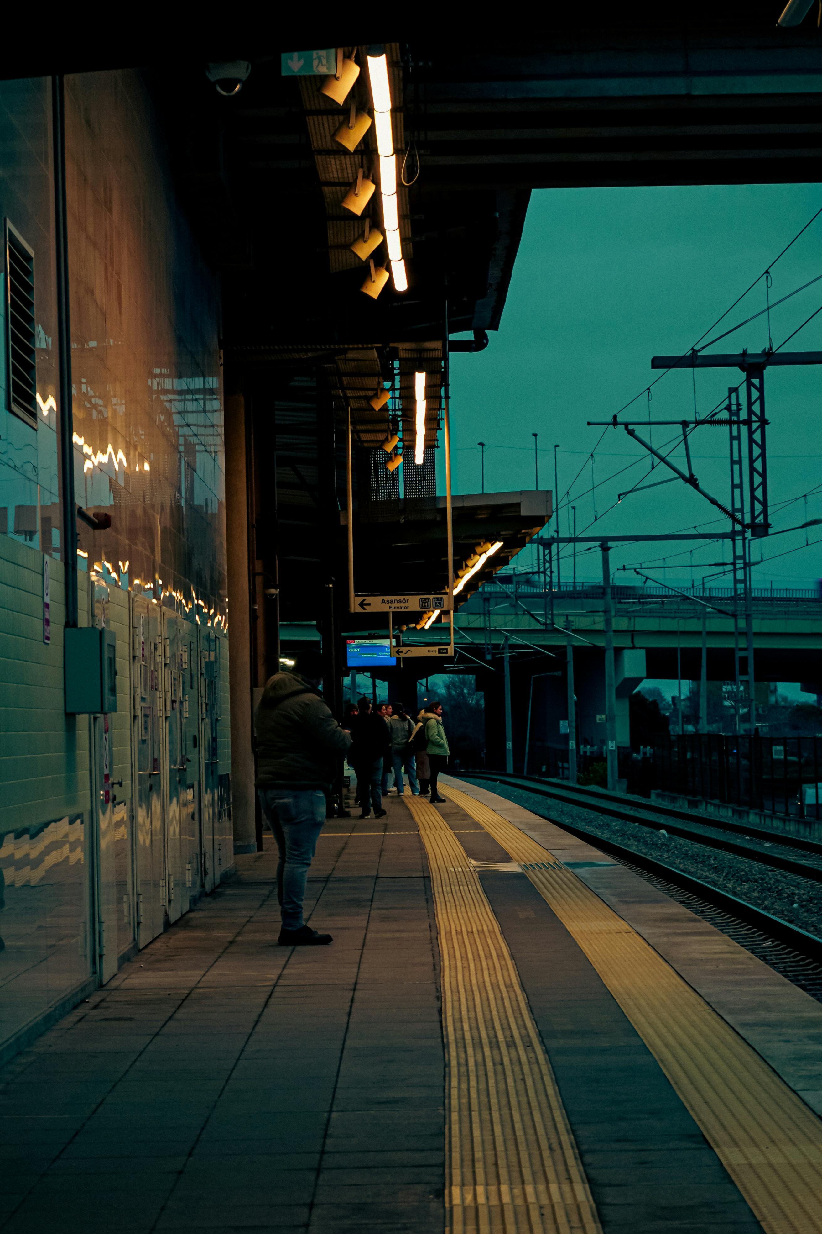 Miễn phí Mọi người đang chờ đợi tại sân ga ngoài trời lúc hoàng hôn, ghi lại khung cảnh đô thị thanh bình. Ảnh lưu trữ