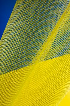 Dynamic abstract image of flowing yellow mesh fabric set against a blue background.