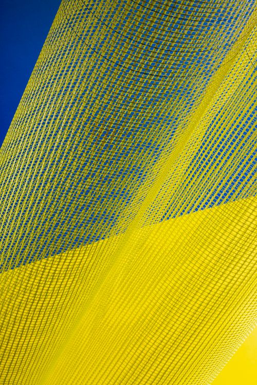 Free Dynamic abstract image of flowing yellow mesh fabric set against a blue background. Stock Photo