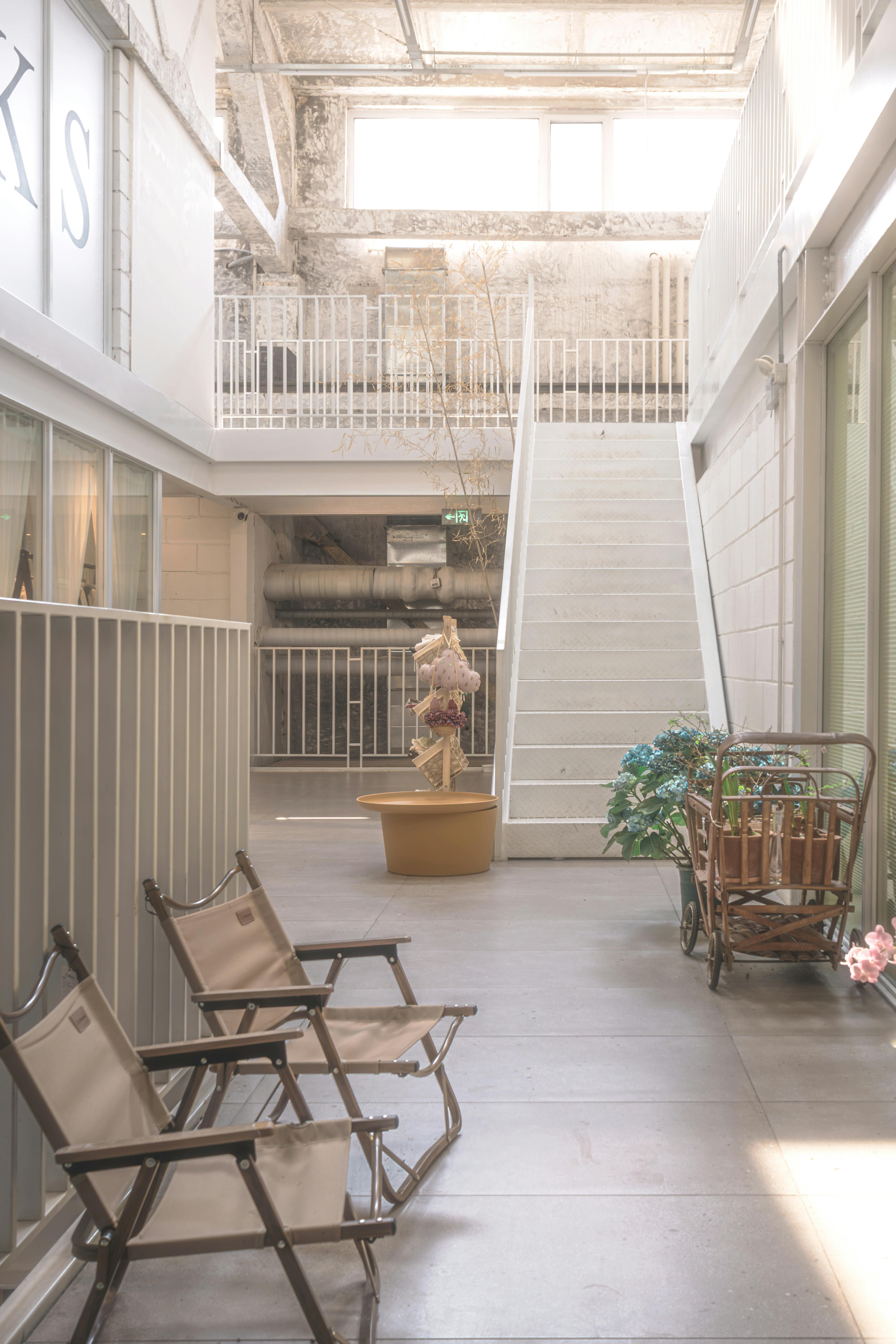 bezplatná Vzdušný pokoj v industriálním stylu s židlemi, velkým schodištěm a jasným osvětlením. Základová fotografie