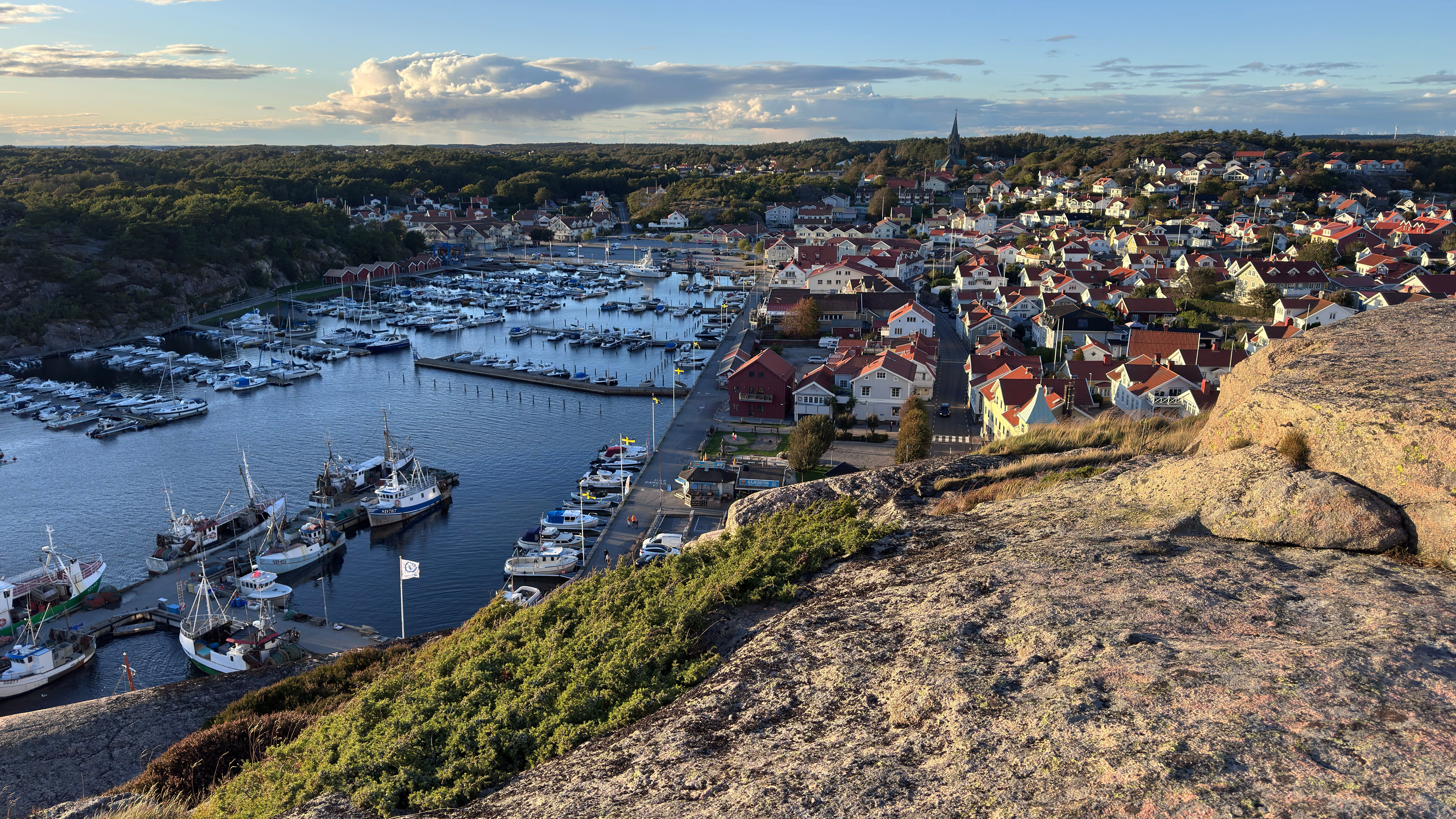 Aerial view of Fjällbacka harbor with boats, hillside, and picturesque townscape.
