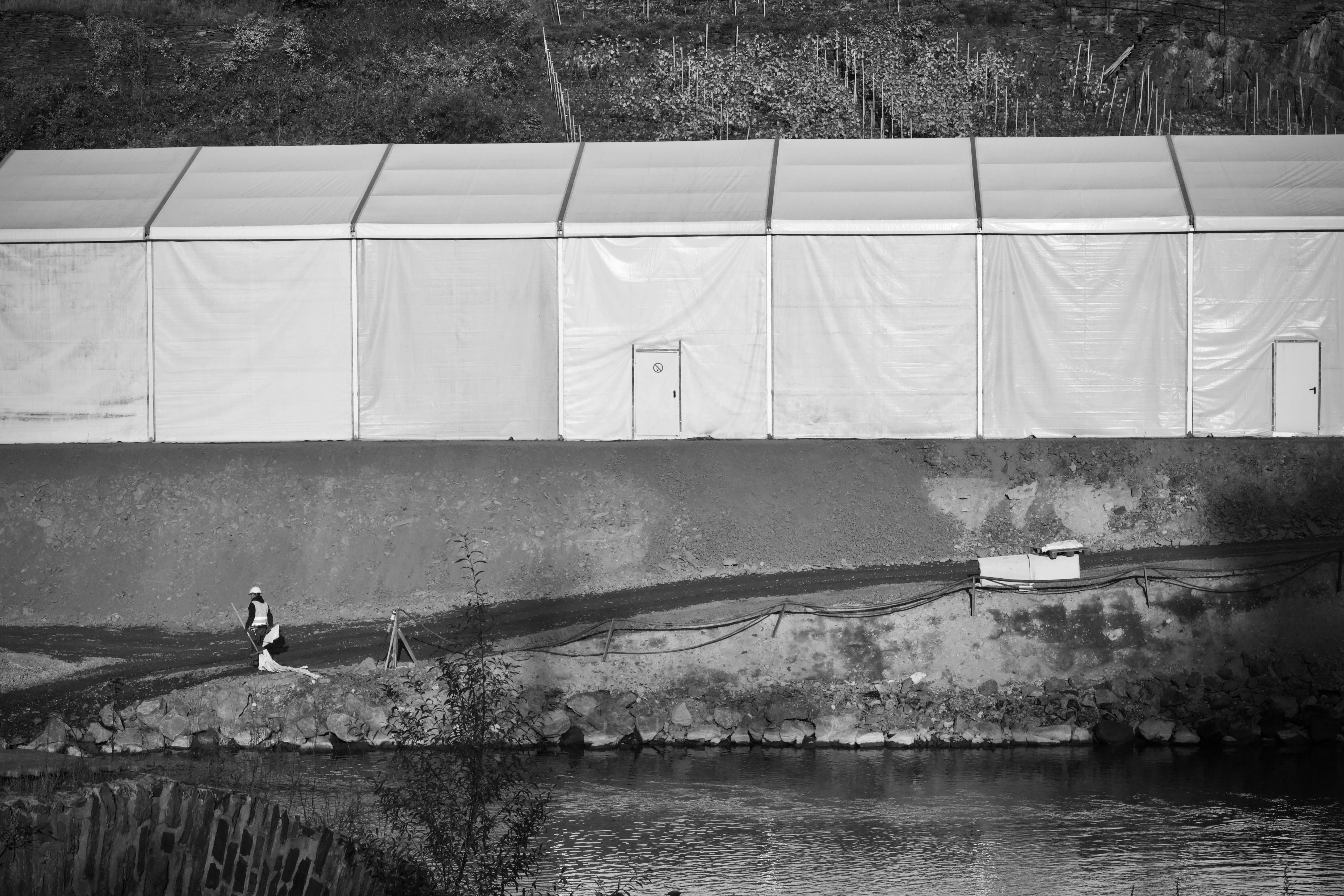 Gratis En enslig skikkelse går forbi et telt nær en elv, fanget i svart-hvitt. Arkivbilde