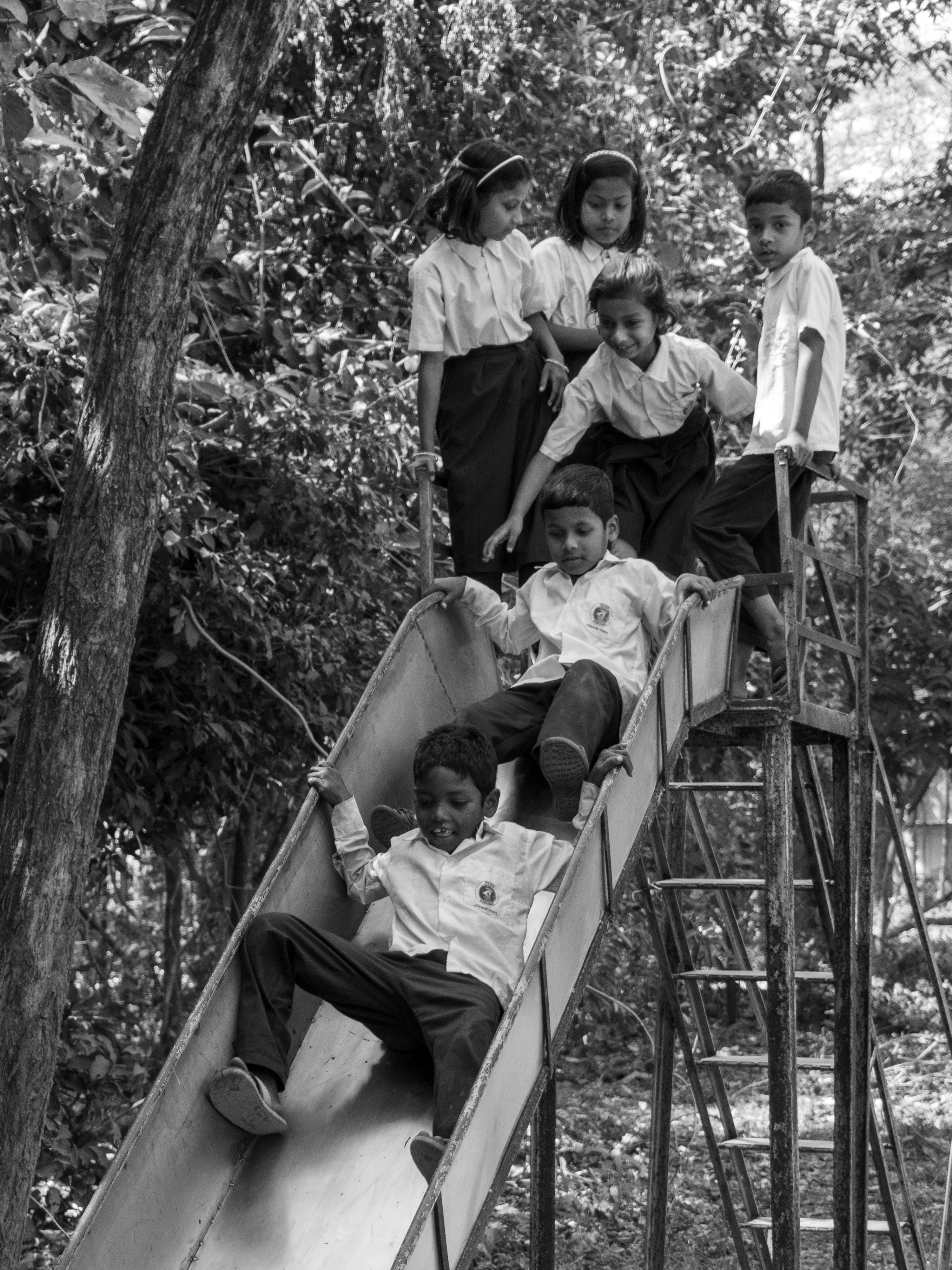 bezplatná Nostalgická scéna s dětmi hrajícími si na kovové skluzavce v parku, zachycená monochromaticky. Základová fotografie