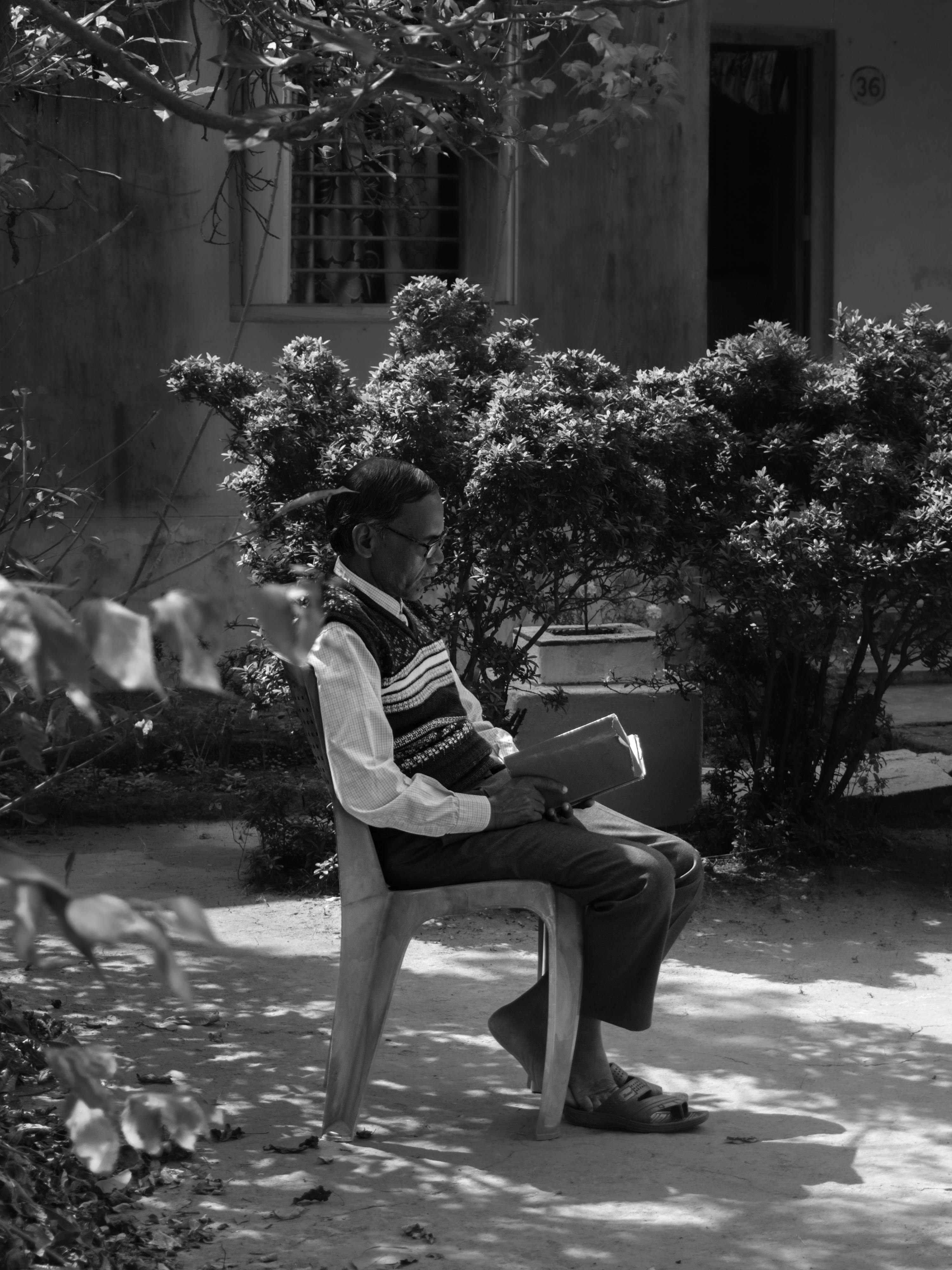 Безкоштовне Чорно-біле зображення старшого чоловіка, який читає в тихому саду. стокове фото