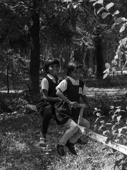 Two children enjoying a seesaw in a natural park setting, captured in black and white.