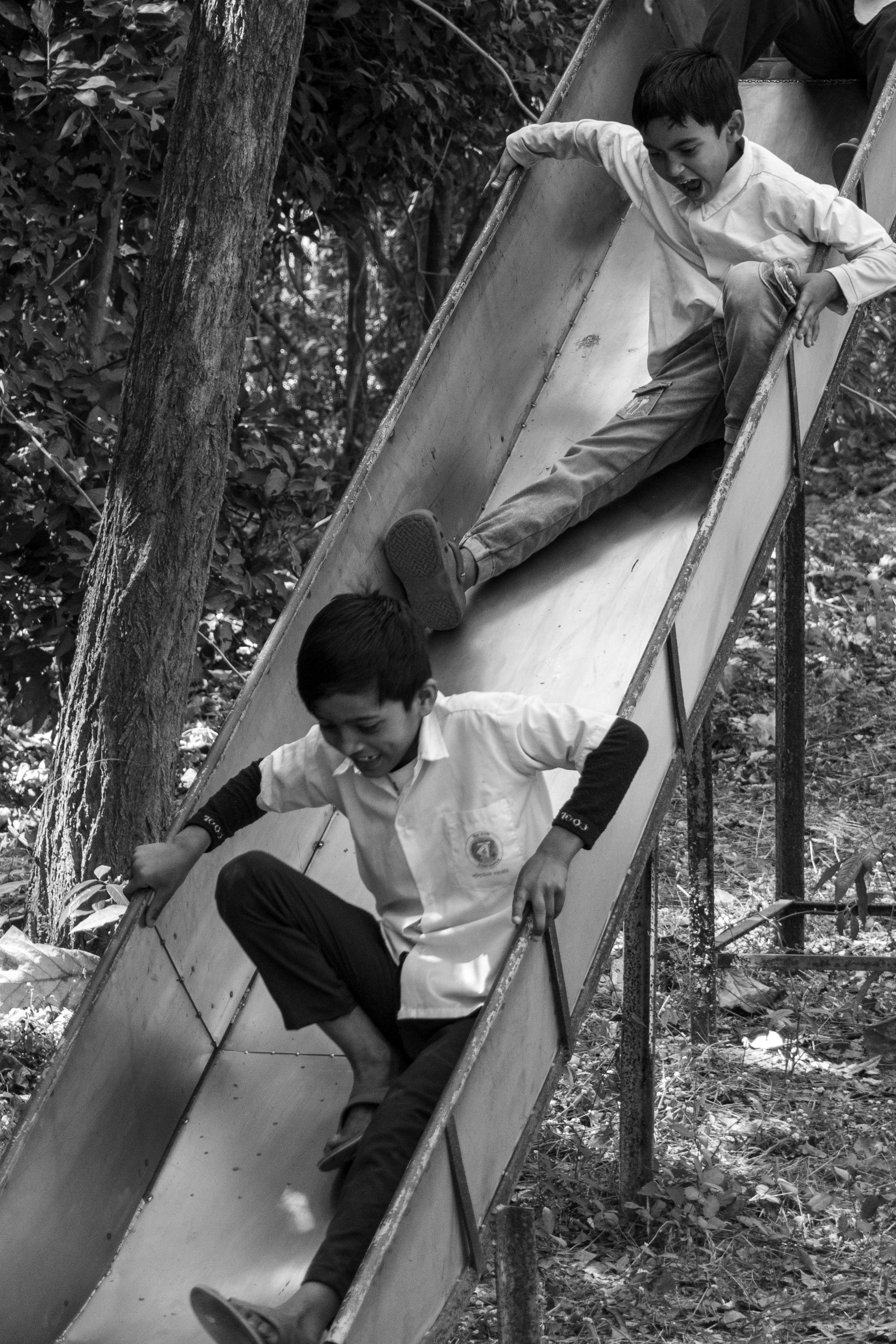 bezplatná Dva mladí chlapci si užívají skluzavku v přírodním venkovním prostředí v černé a bílé. Základová fotografie