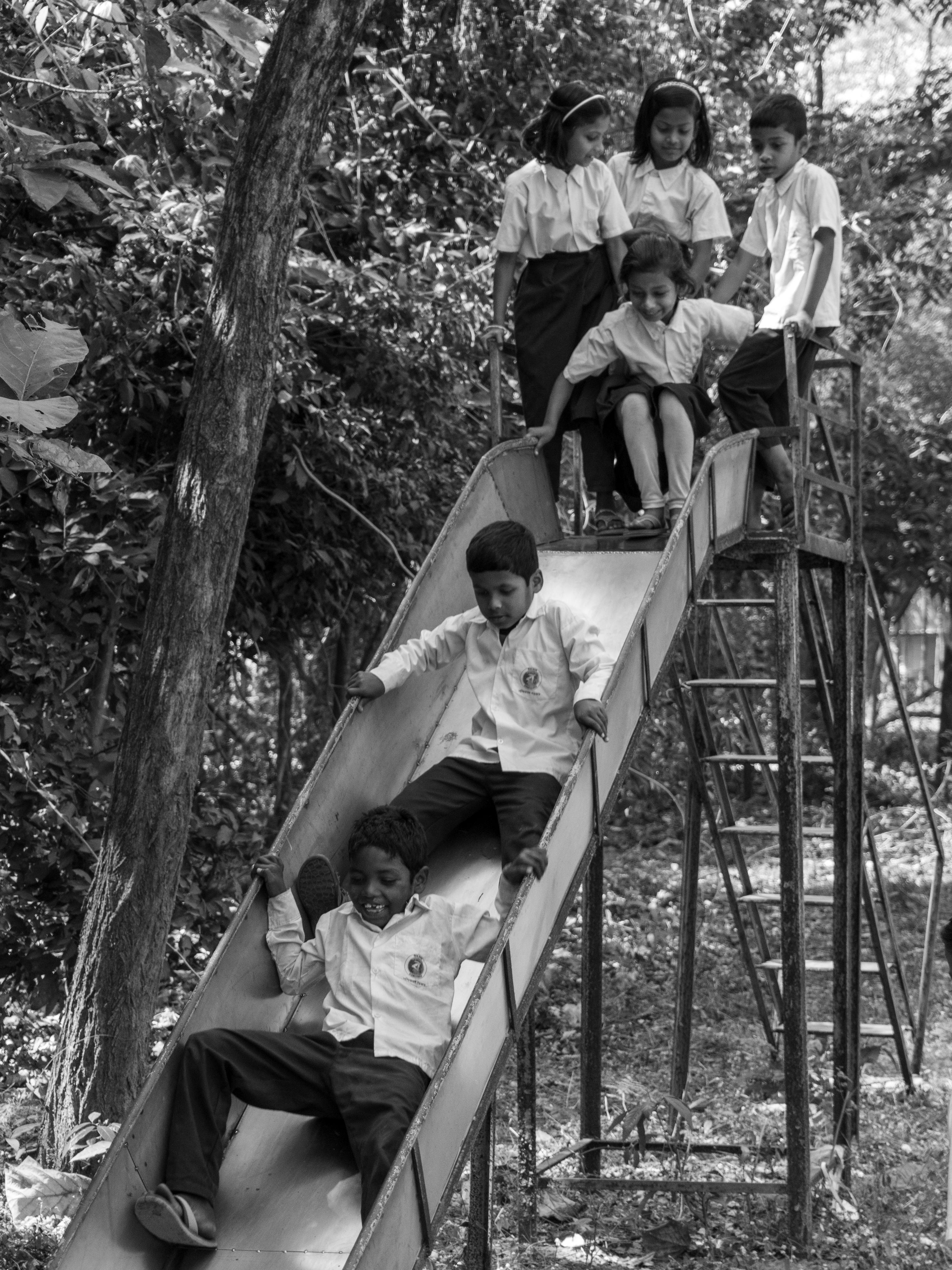 bezplatná Radostná skupinka dětí hrajících si na skluzavce na venkovním hřišti, zachycená černobíle. Základová fotografie