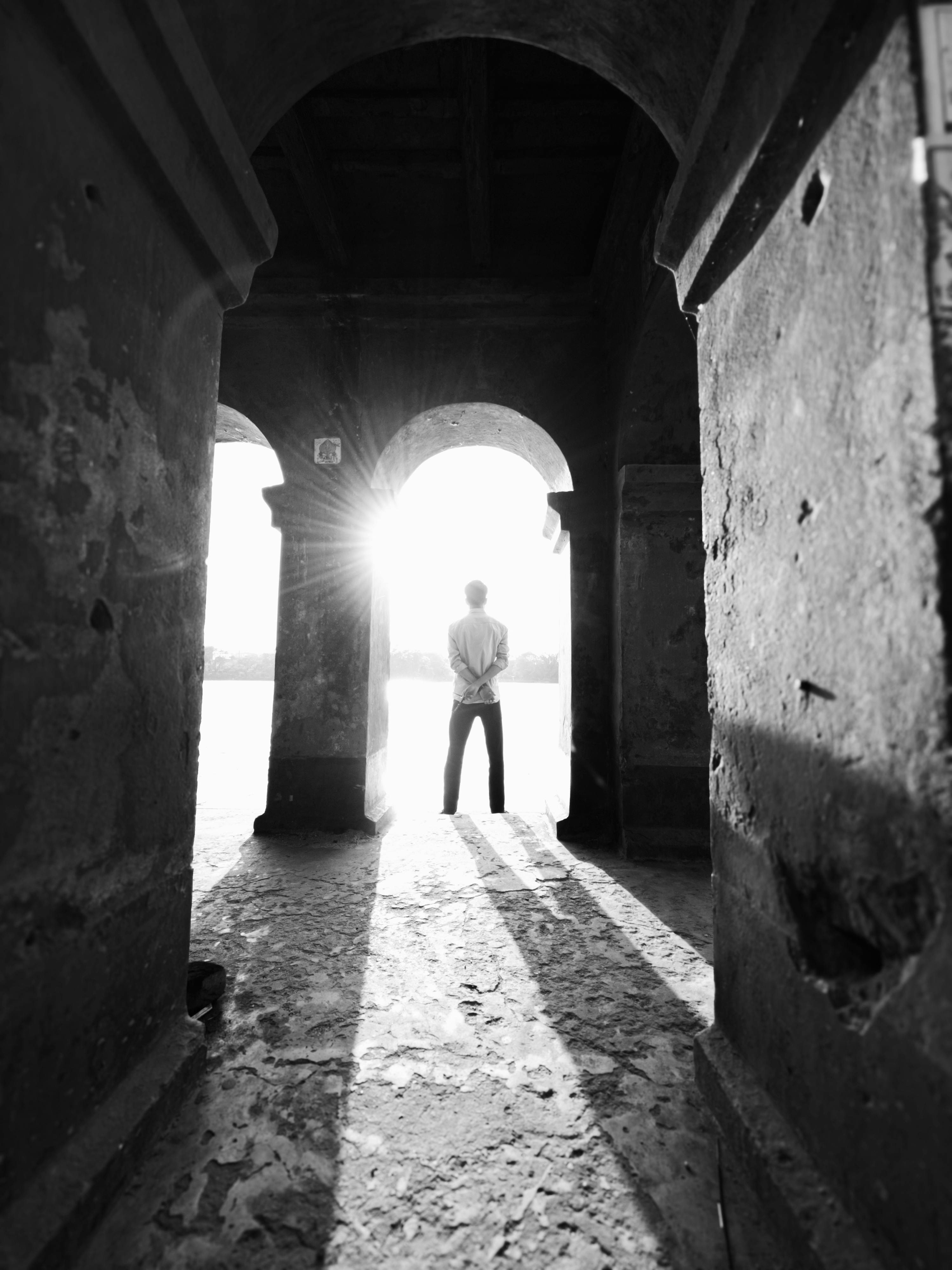 免费 阳光透过古老的石拱门照射进来，映衬着站在拱门前的行人剪影。 素材图片