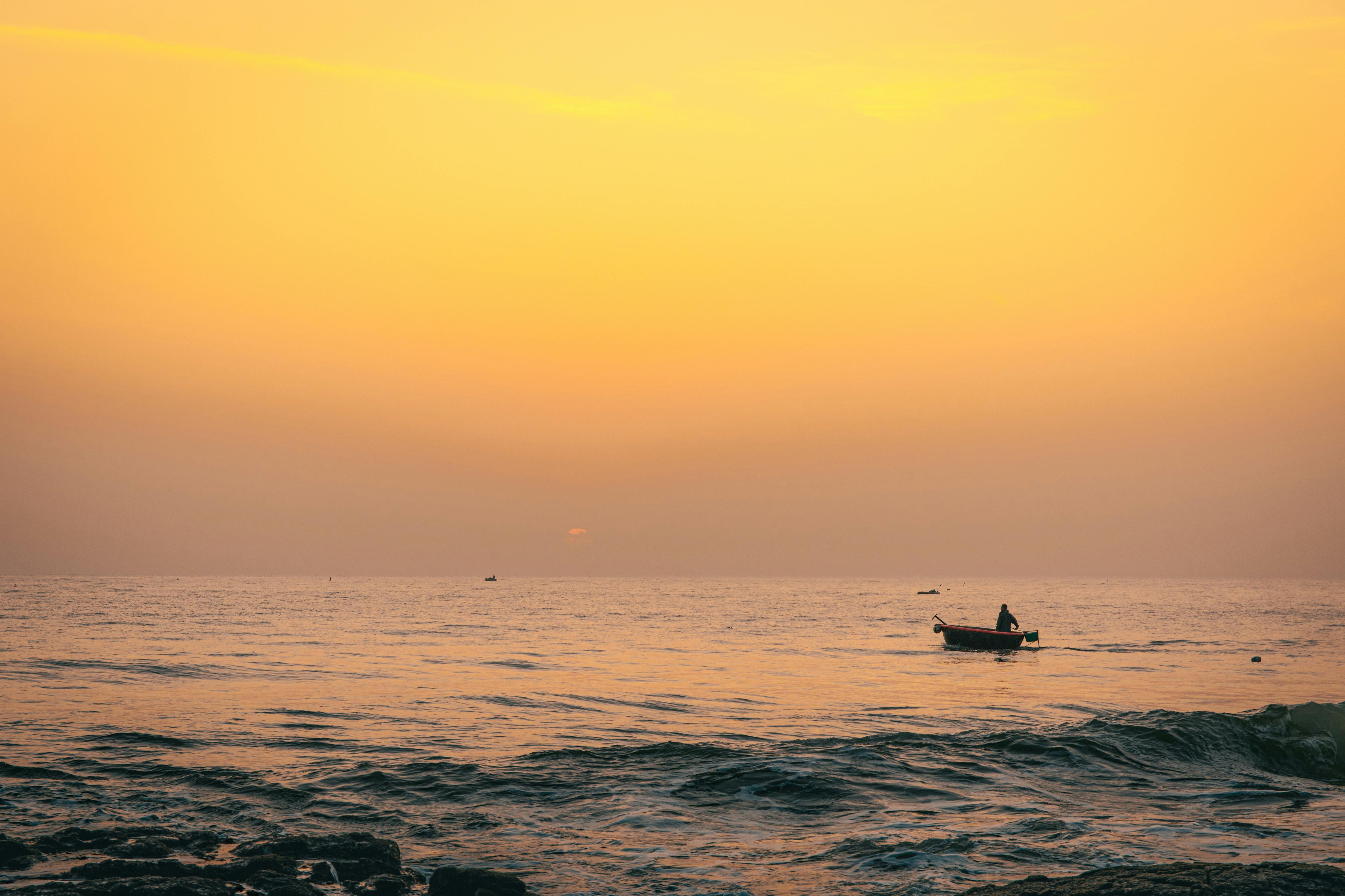 бесплатная На закате в океане одинокая лодка плывет по воде, создавая безмятежную и умиротворяющую картину. Стоковое фото