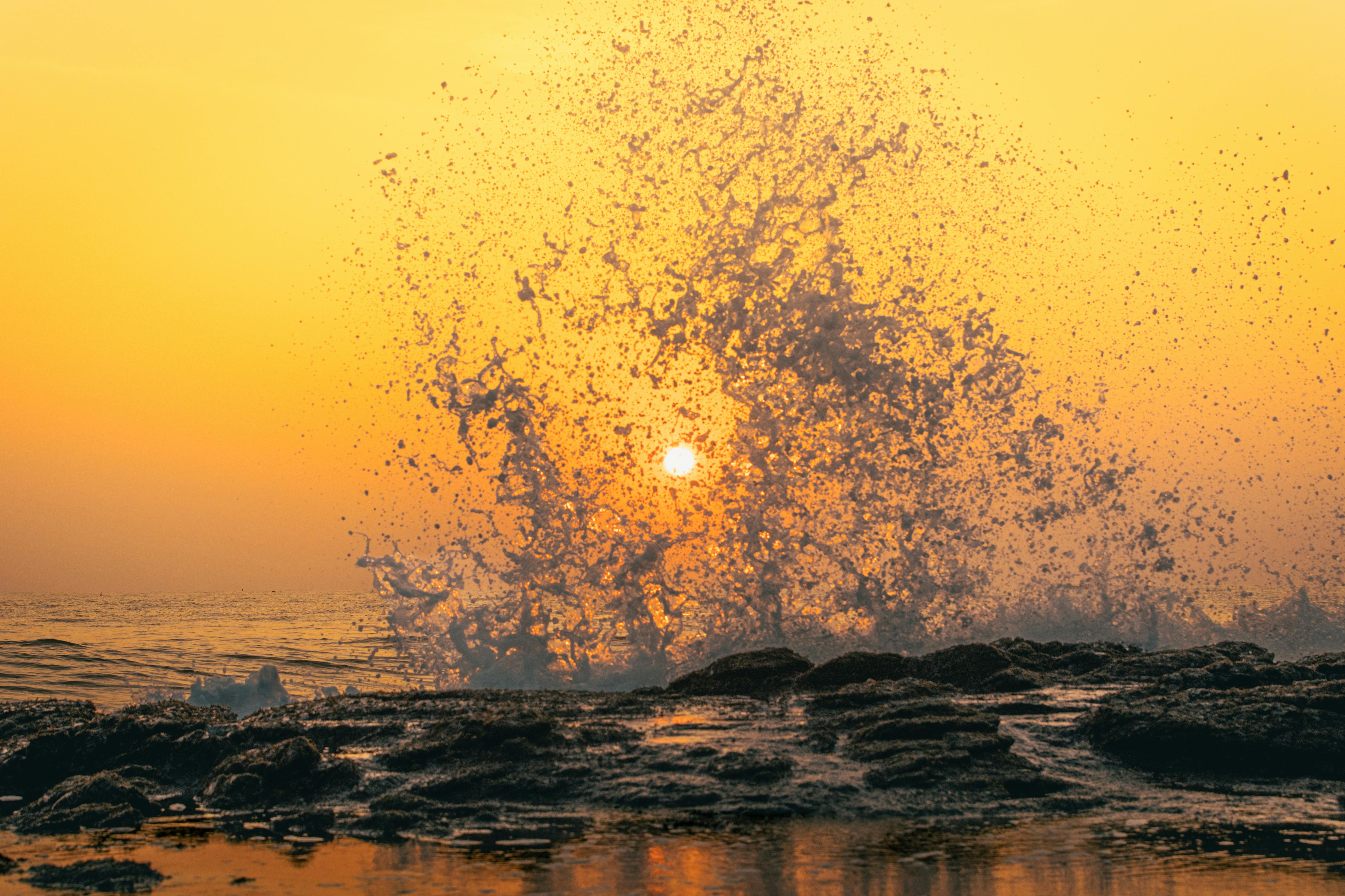 Ücretsiz Arka planda sıcak ve canlı bir gün batımıyla birlikte, okyanus dalgalarının kayalara çarpma sesinin büyüleyici görüntüsü. Stok Fotoğraflar