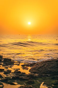 Vibrant sunrise over an ocean with rocky shore reflections, creating a serene ambiance.