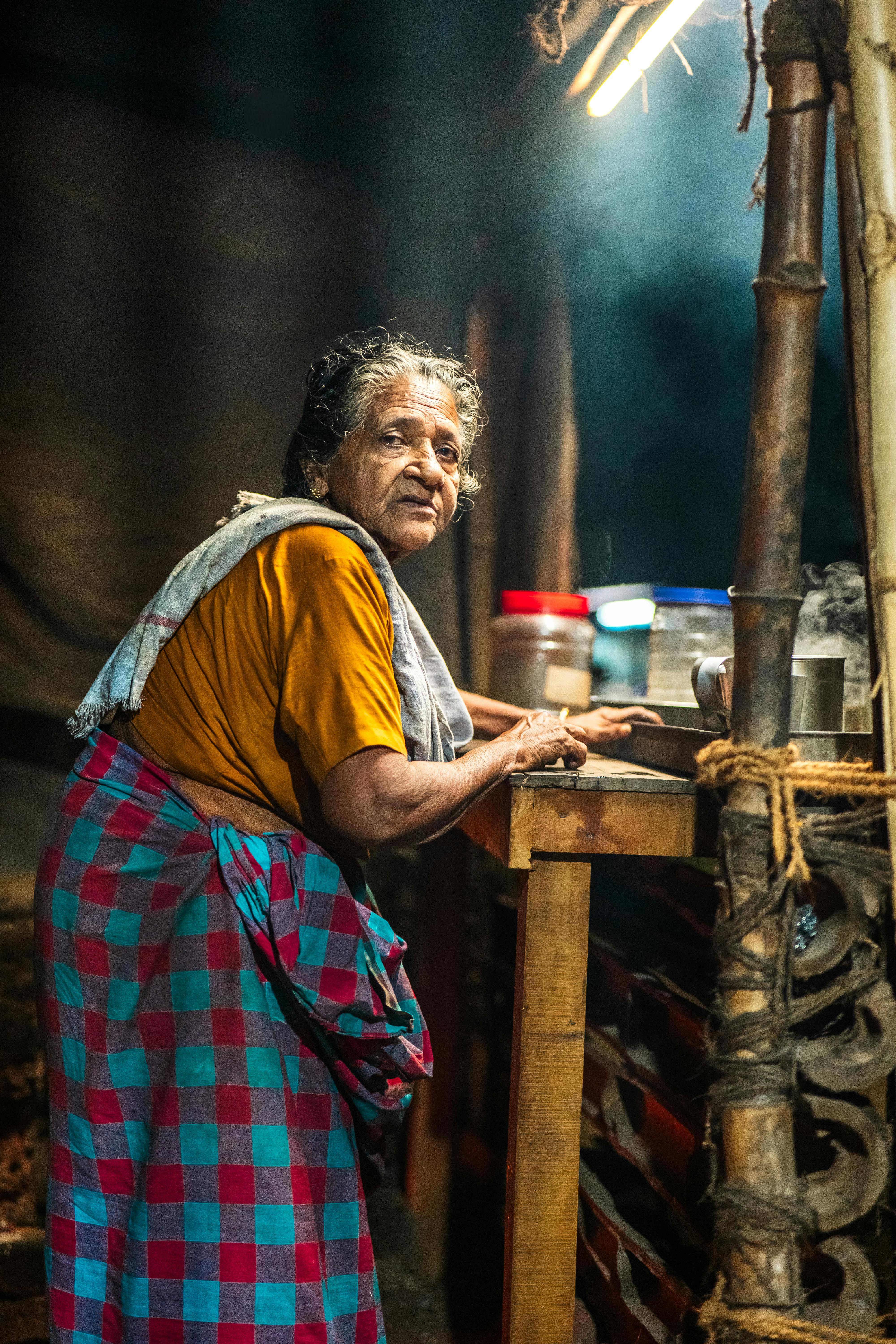 Bezpłatne Starsza kobieta gotuje w rustykalnej kuchni w ciągu dnia, wśród dymu i tradycyjnych dekoracji. Zdjęcie z galerii