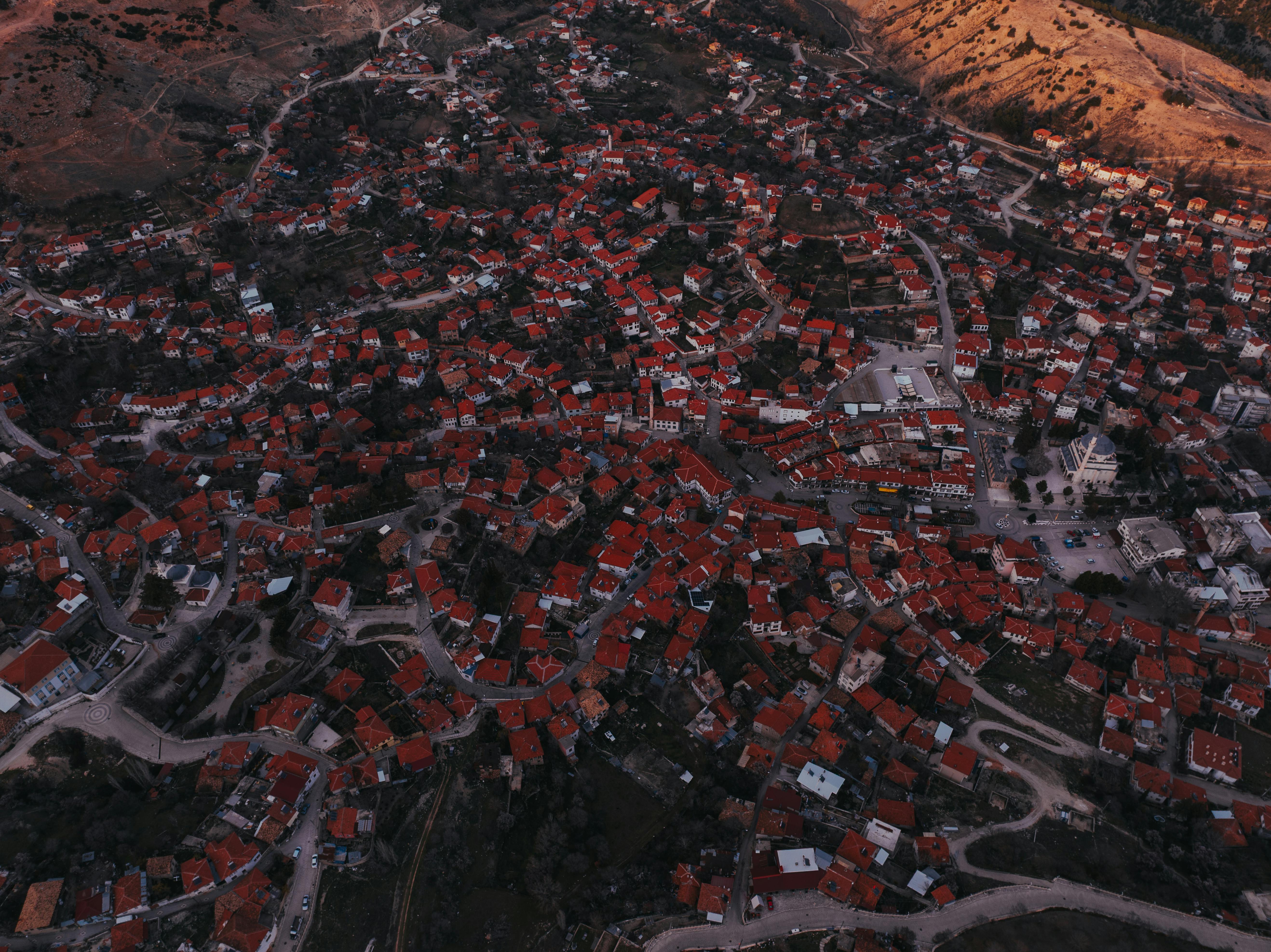 grátis Fotografia aérea que captura uma extensa vila com telhados vermelhos contra um fundo crepuscular. Foto profissional