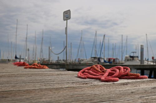 Free Red ropes on a wooden dock with sailboats in the background under a cloudy sky. Stock Photo