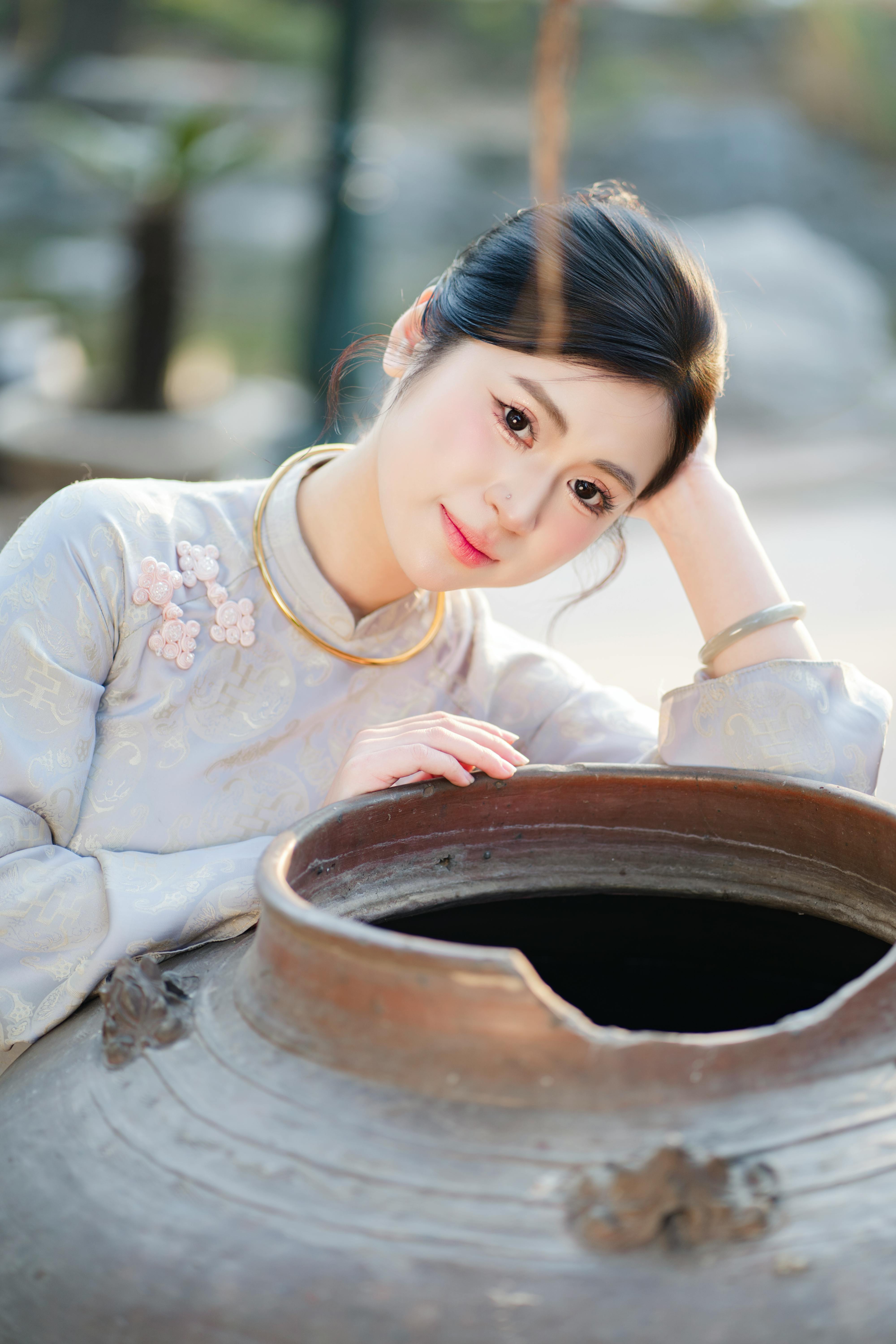 無料 伝統的な衣装を着た女性が、屋外の大きな植木鉢の横でポーズをとっている。 写真素材