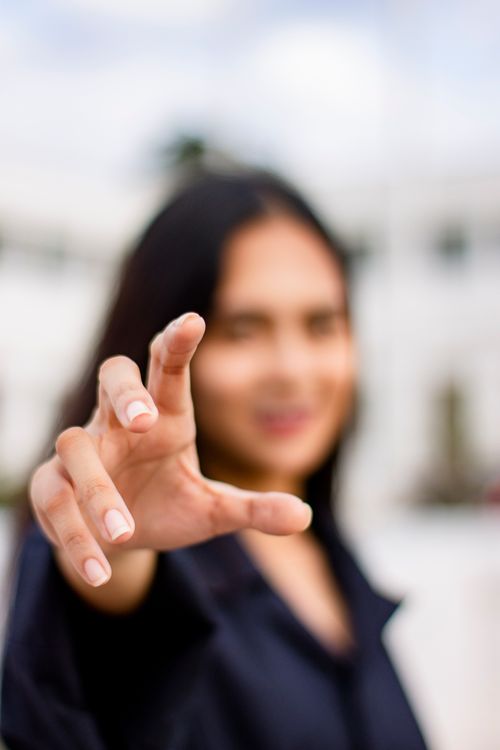 Free Unrecognizable young woman with long dark hair smiling and reaching out hand towards camera Stock Photo