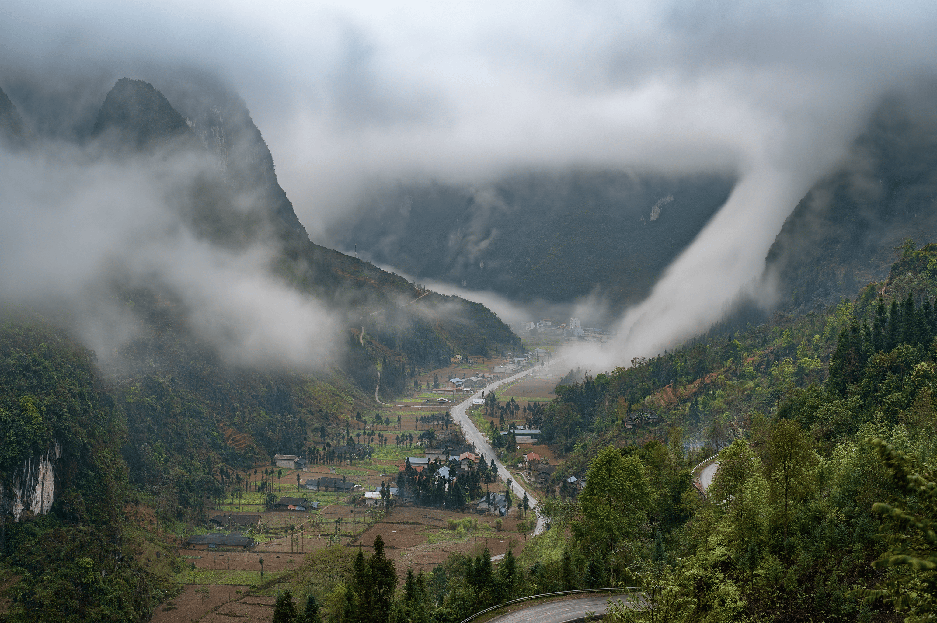 Gratis Naturskjønn, tåkete fjelldal med en svingete vei og frodig grøntområde. Arkivbilde